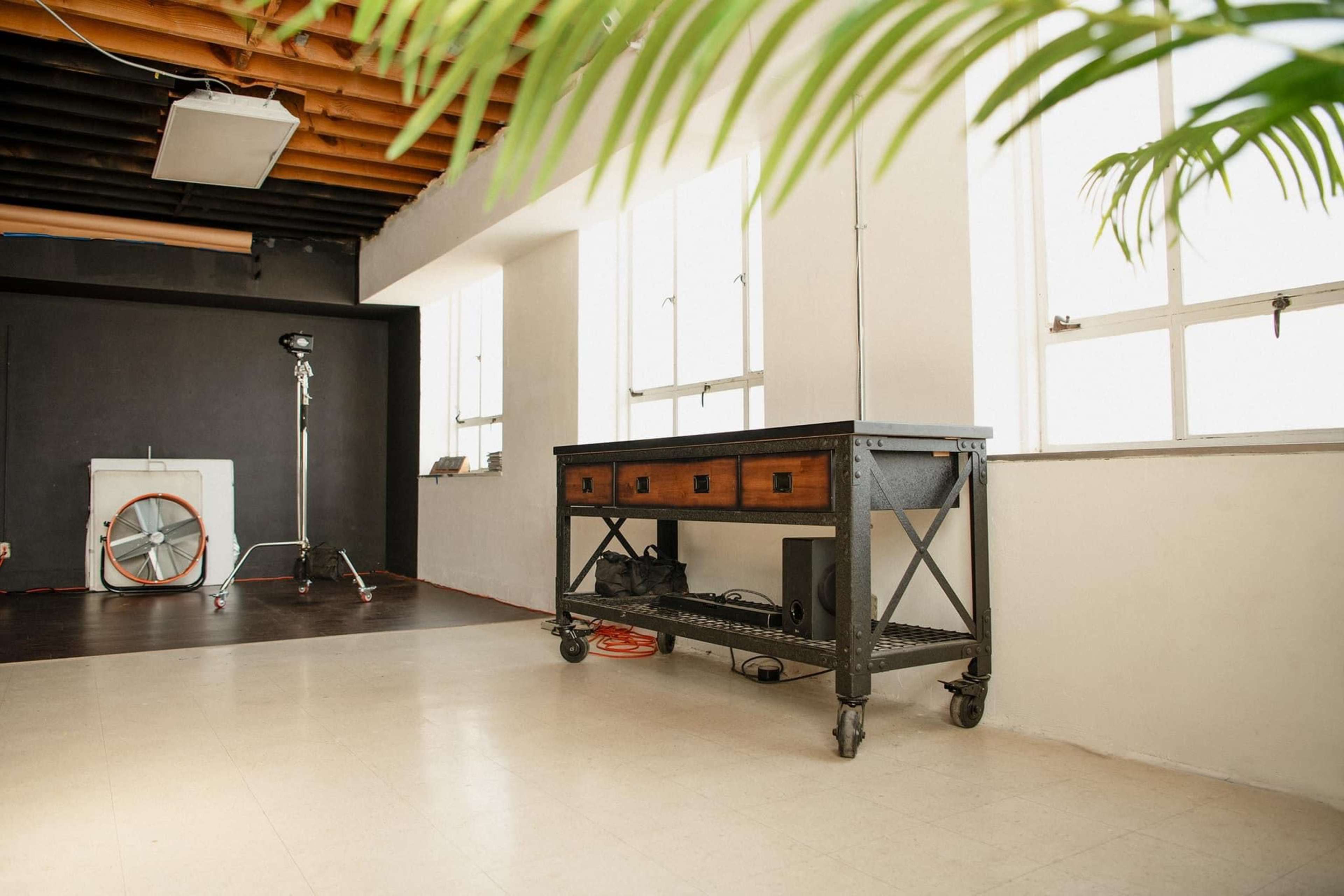 A spacious studio with a metal table on wheels, large windows, and a backdrop setup in the corner.
