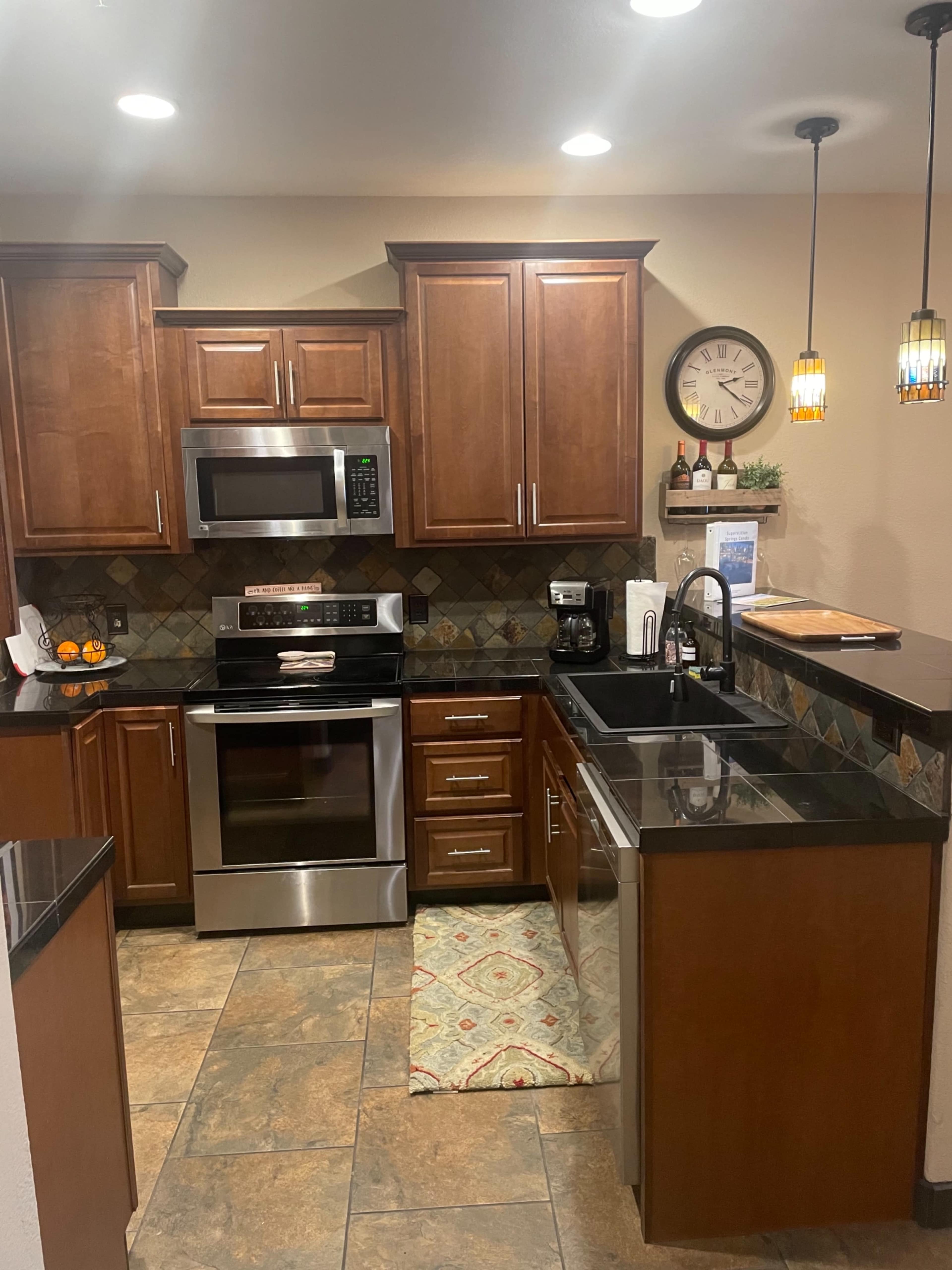 The image shows a modern kitchen with dark wood cabinetry, stainless steel appliances, and a black countertop.