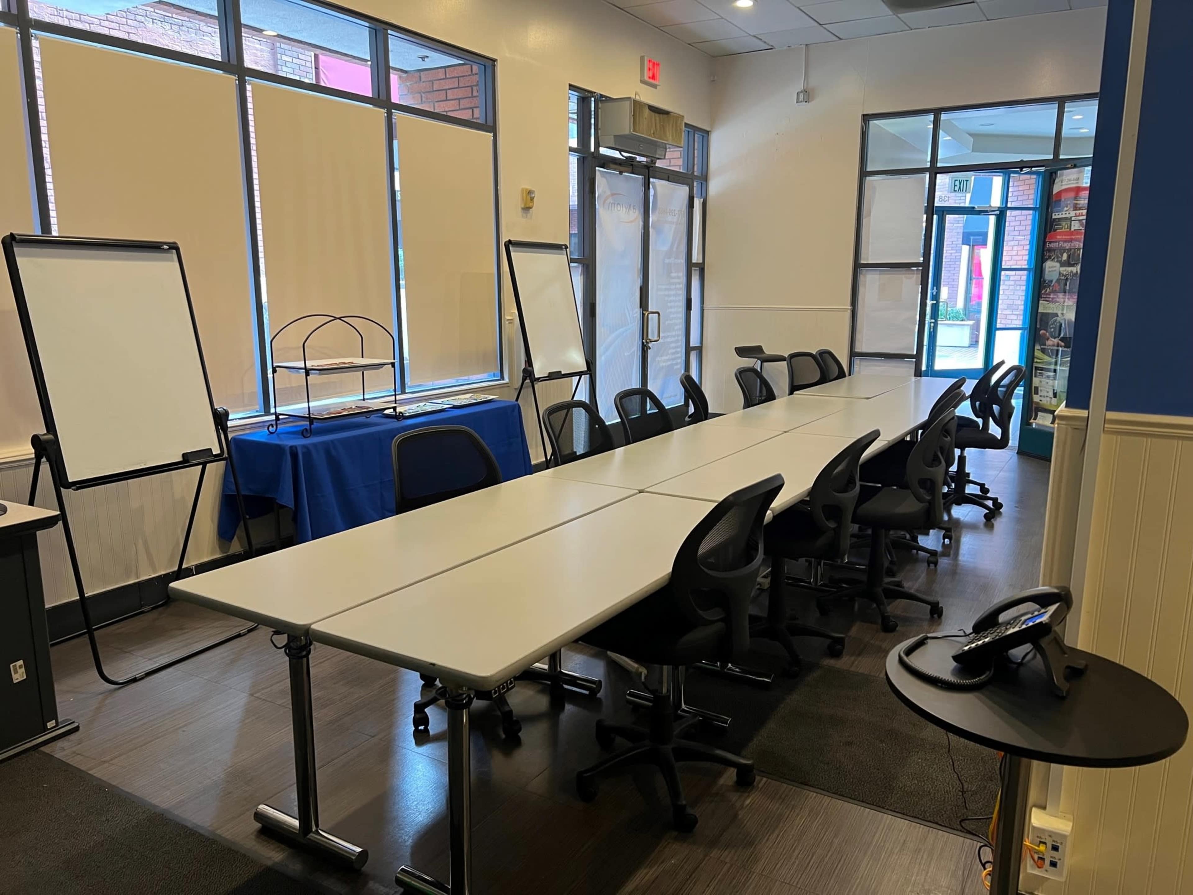 A large meeting room features a long table with chairs, a presentation board, and a doorway leading to the outside.
