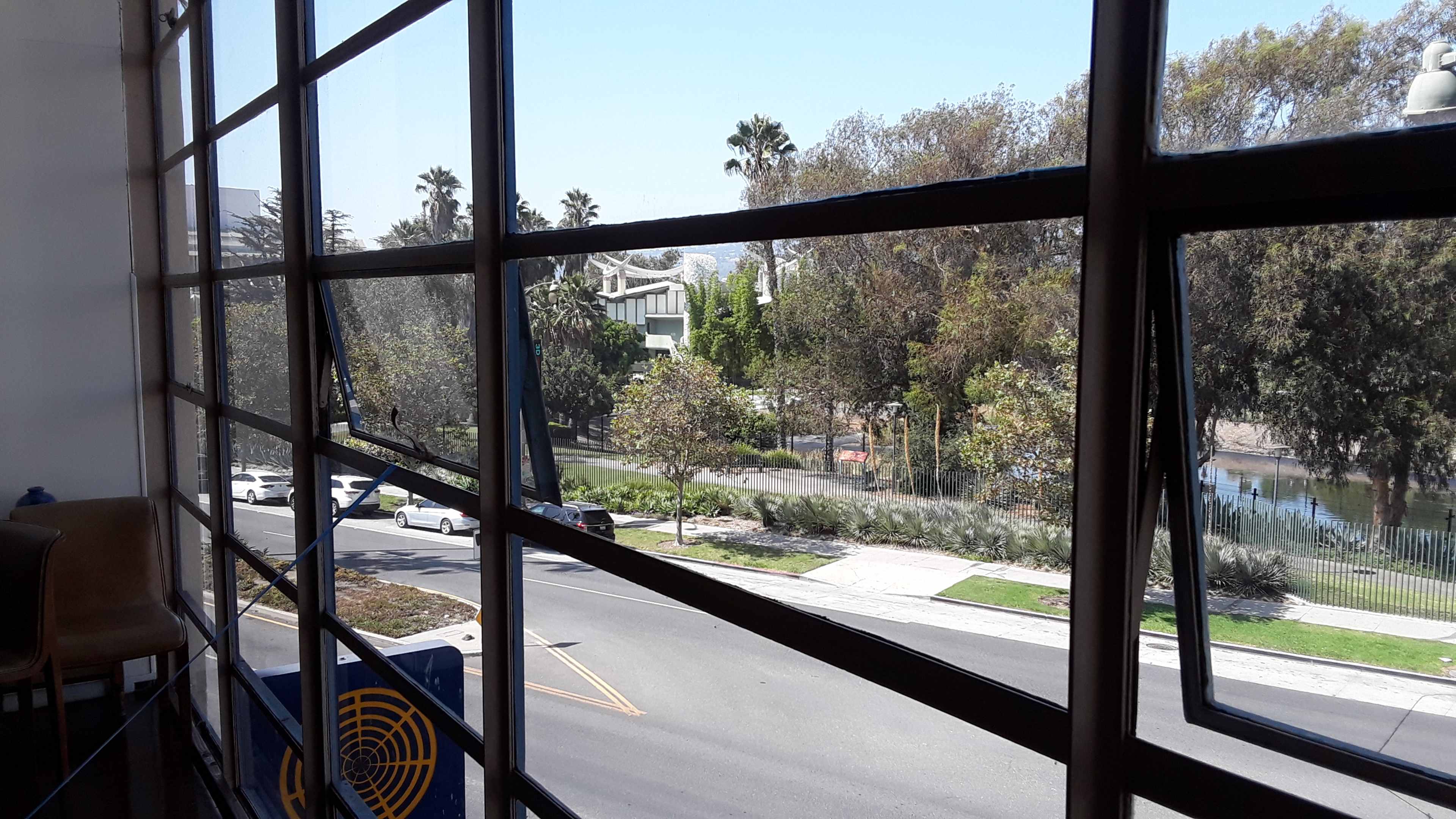 A view through a large window, framing a street lined with trees and parked cars outside.