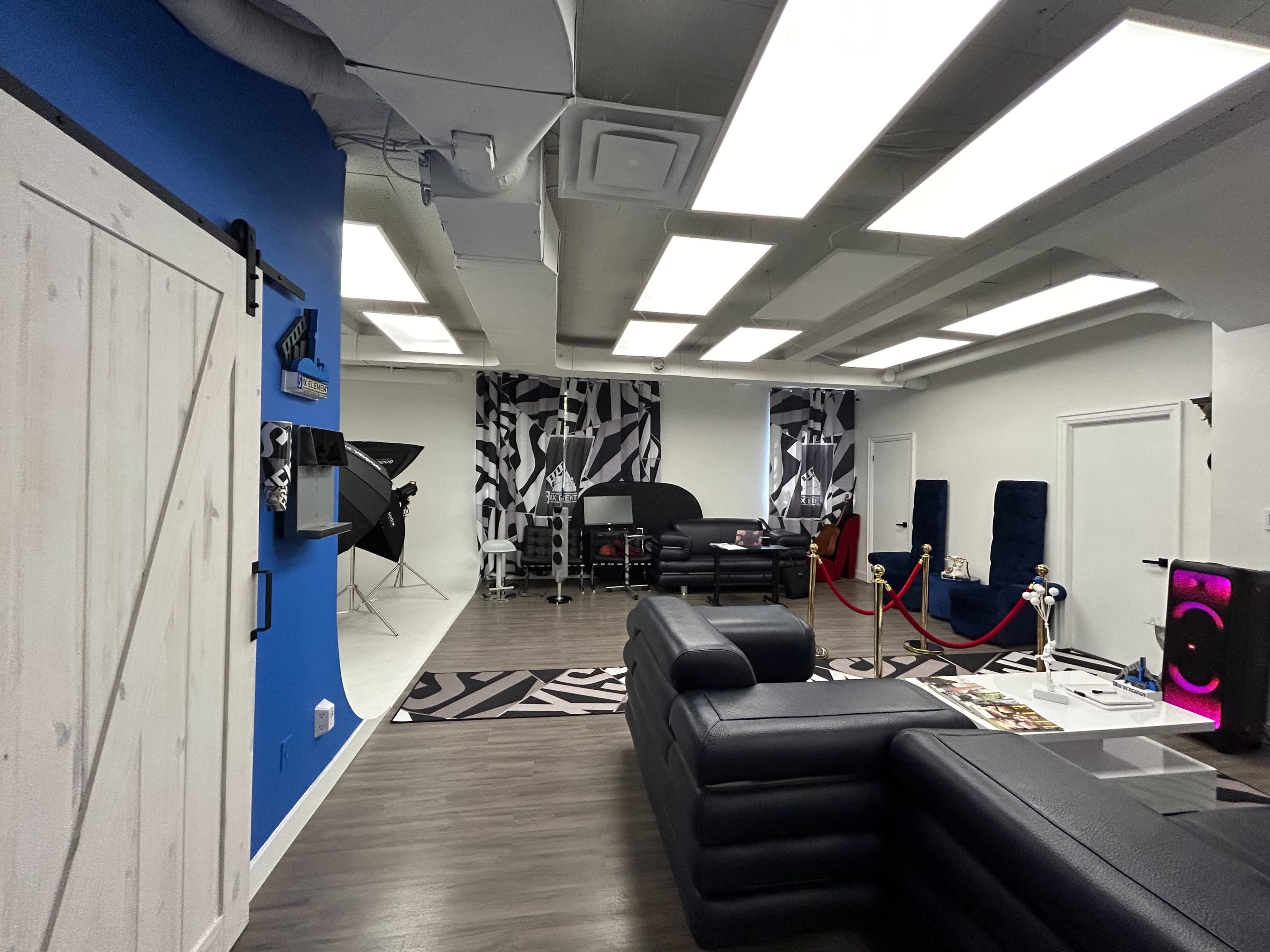 A modern studio space with black leather furniture, vibrant blue walls, and patterned black and white accents, featuring various equipment set up for photography or video production.