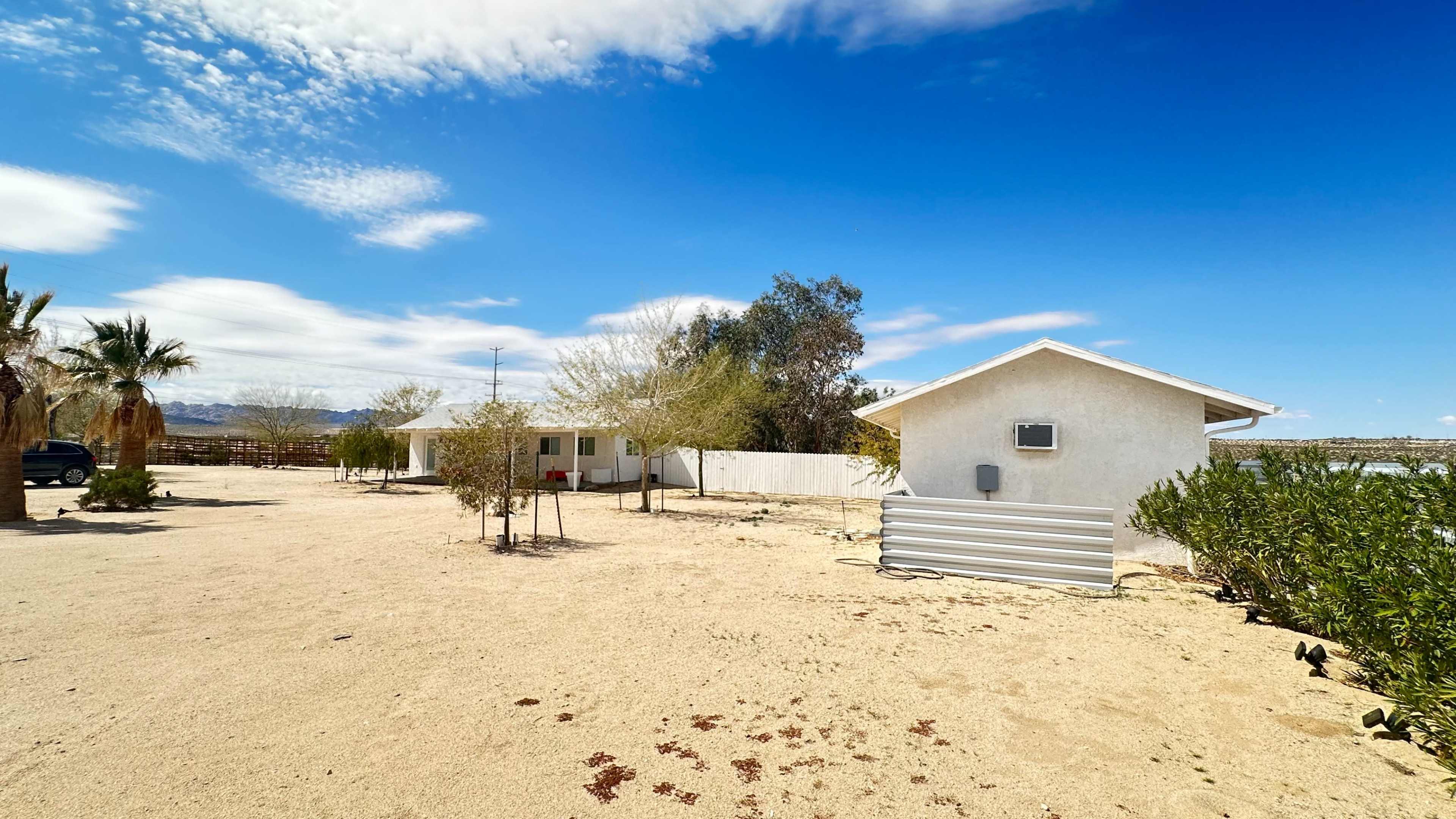 A sandy area features two houses surrounded by sparse vegetation against a blue sky with scattered clouds.