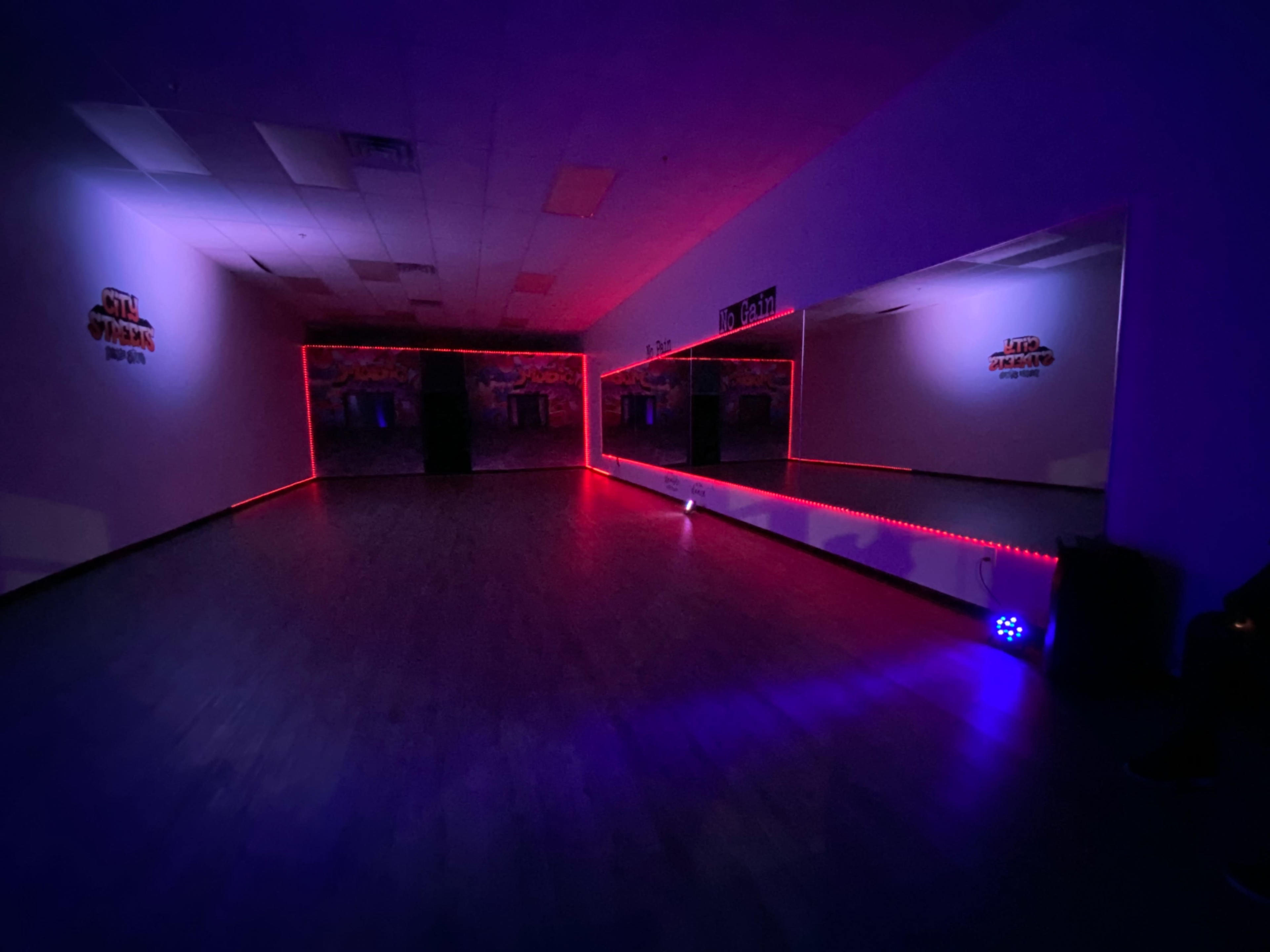 A dimly lit dance studio features a mirrored wall and illuminated edges with blue and red lighting.