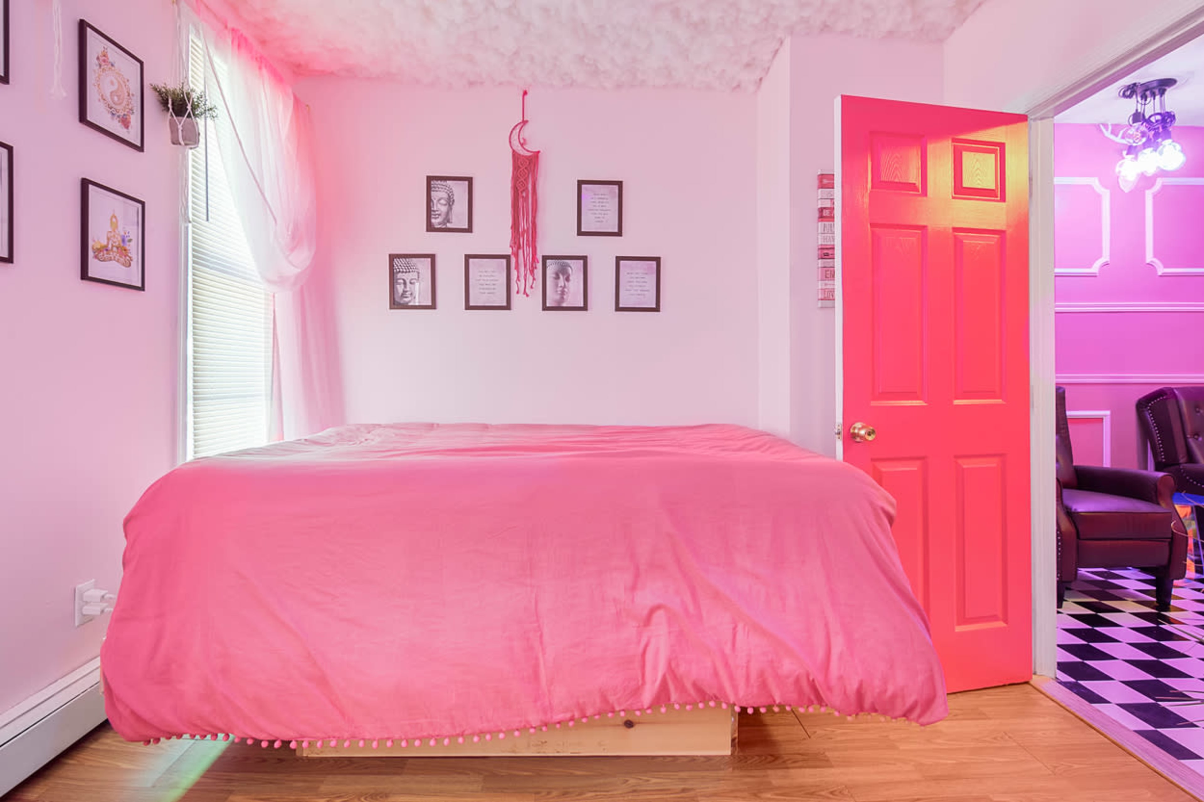 A bright pink bedroom with a large bed covered in a pink comforter and framed artwork on the walls.