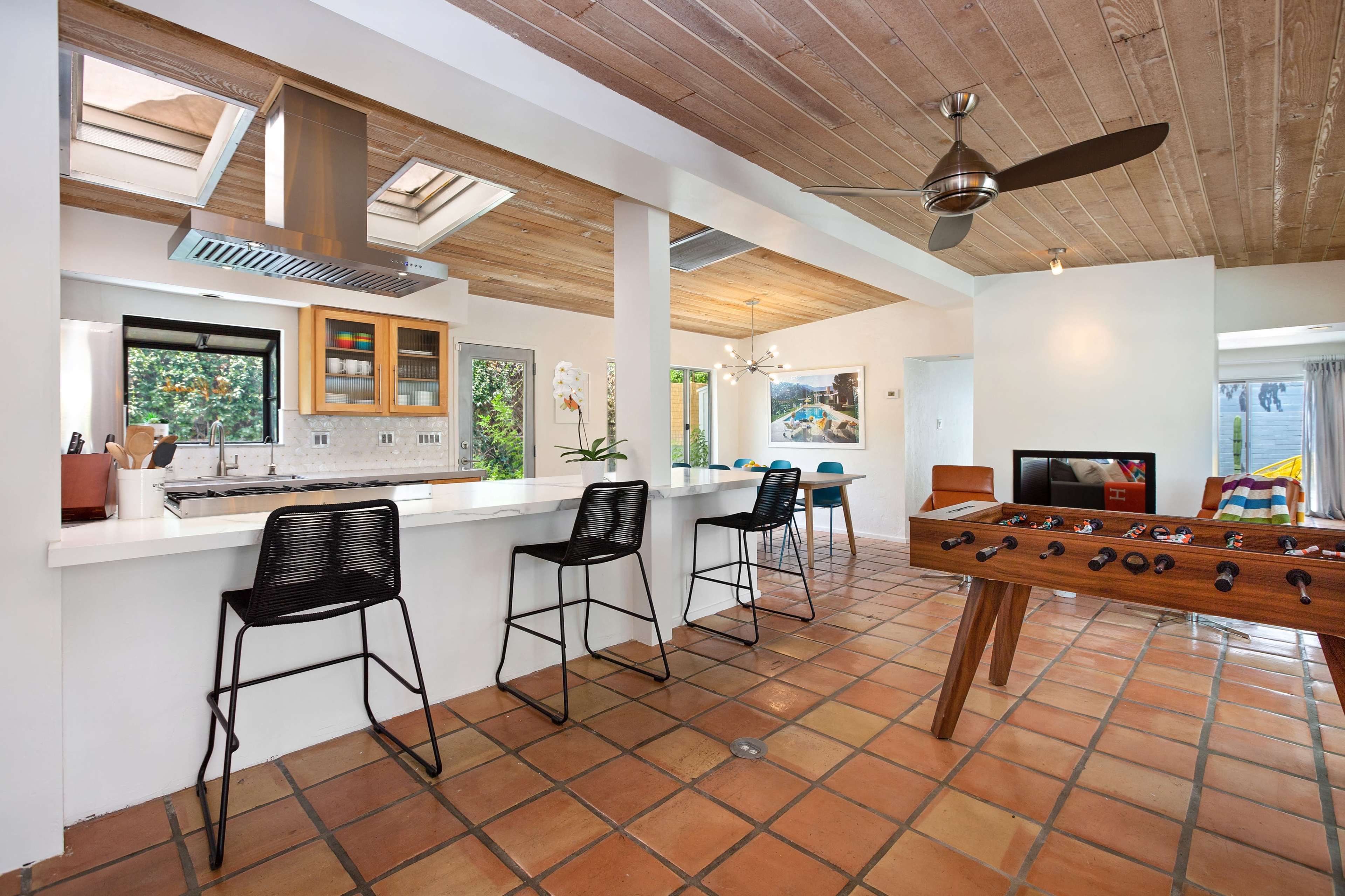 A modern kitchen and living area with a tiled floor, bar seating, and a foosball table.