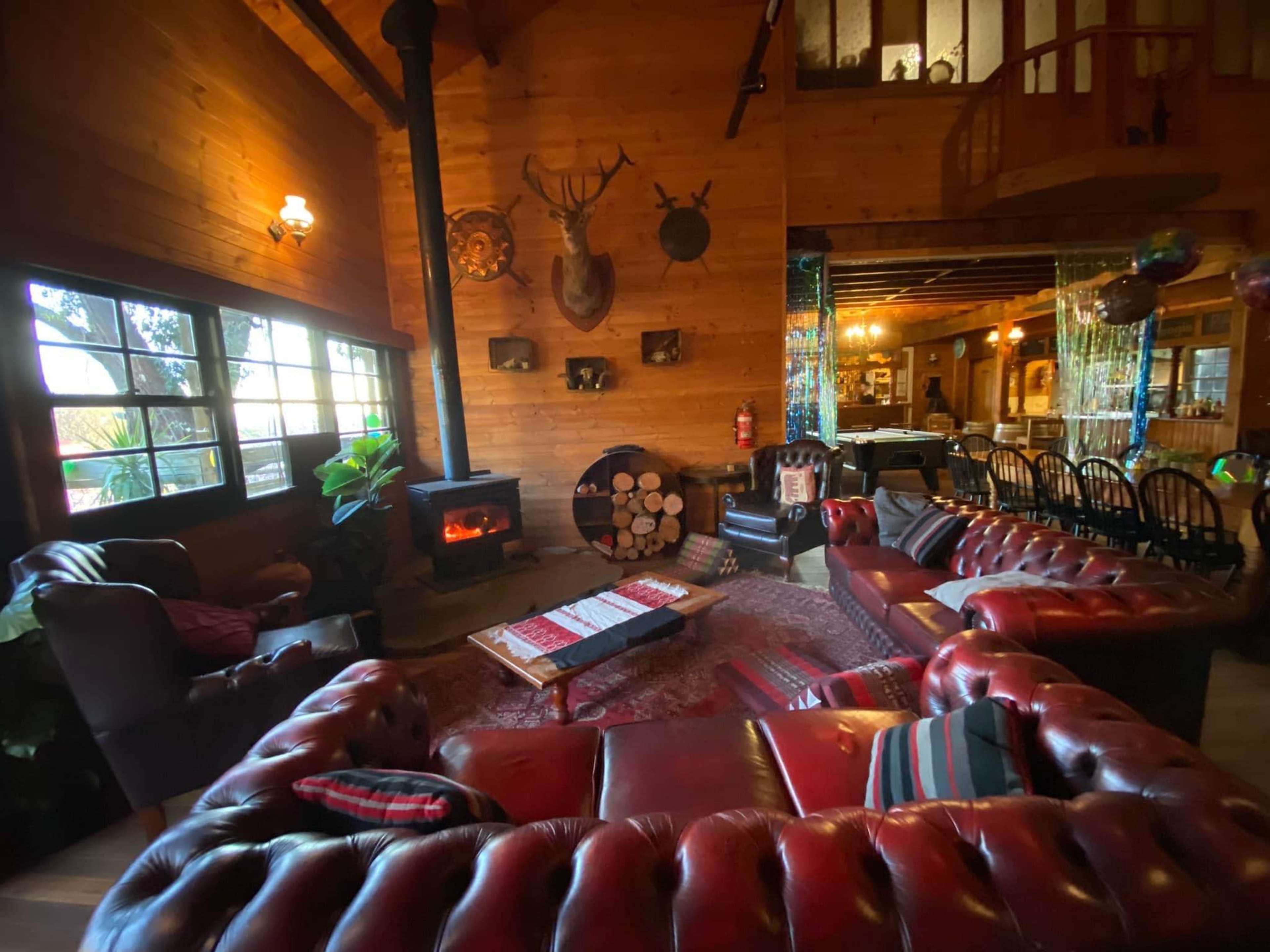 A cozy wooden lounge with leather sofas arranged around a coffee table, a stove, and various decorative elements on the walls.