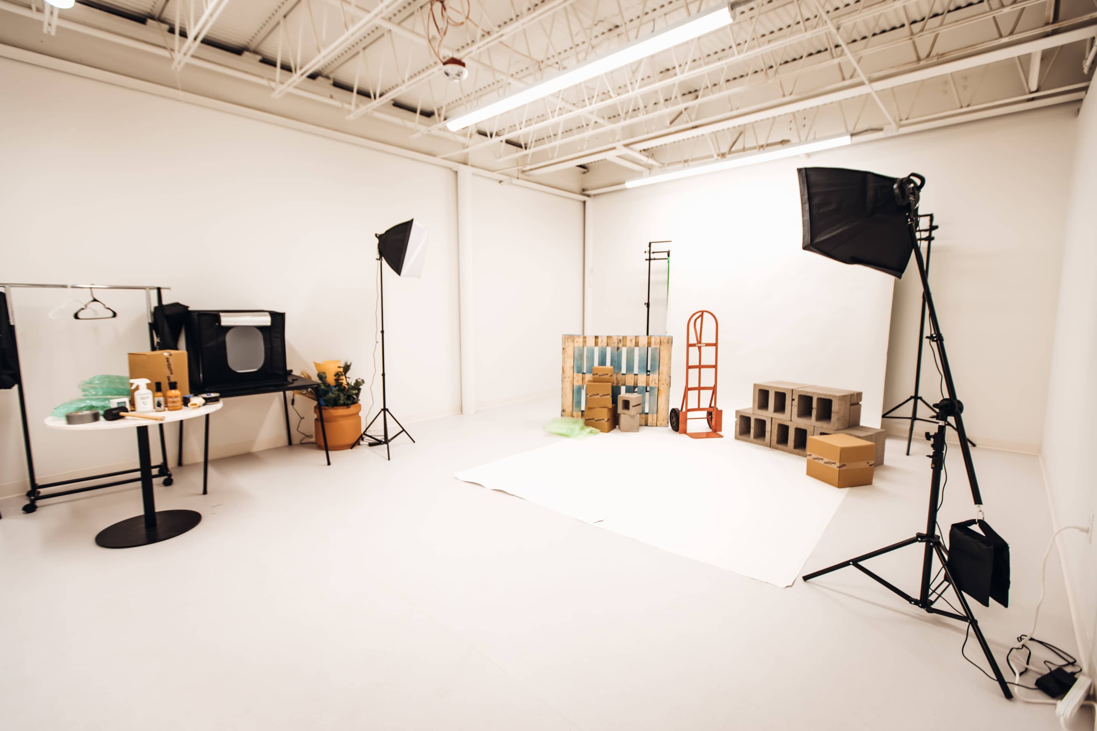 A well-lit studio space equipped with photography lighting, a clothing rack, and various props arranged against a plain backdrop.