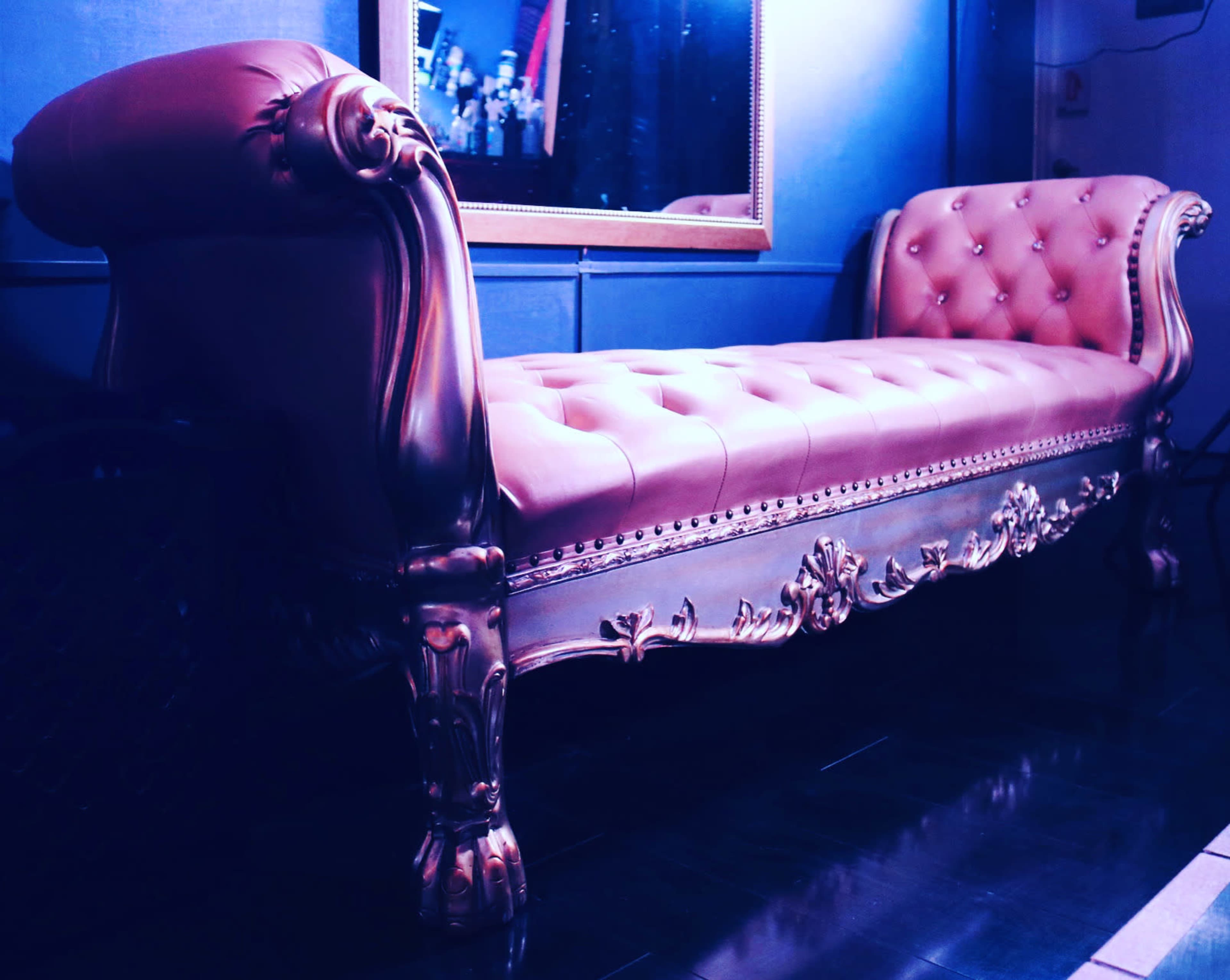 An ornate, burgundy chaise lounge with tufted upholstery and decorative woodwork against a dark background.