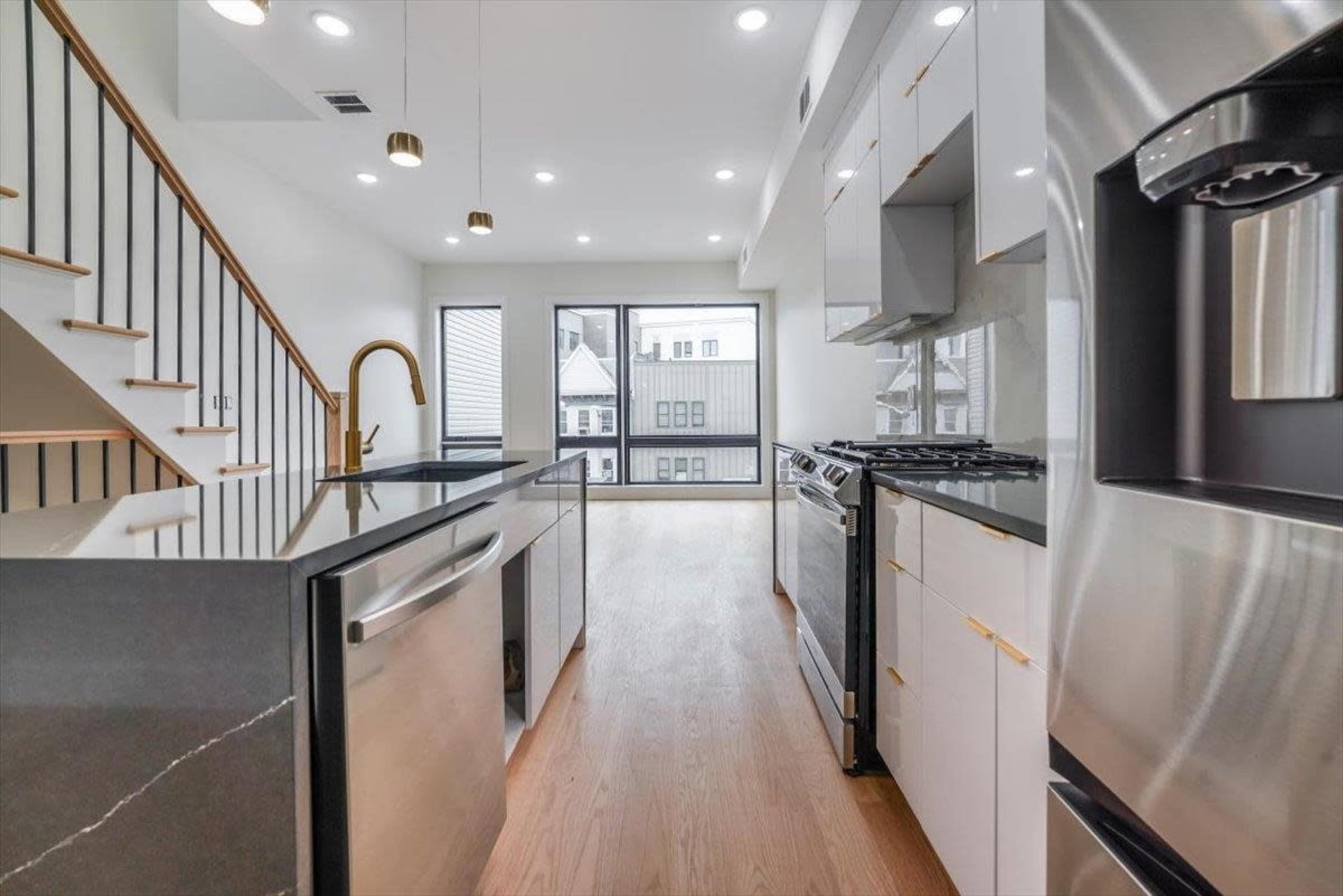 The image shows a modern kitchen with stainless steel appliances, an island, and large windows overlooking a balcony.