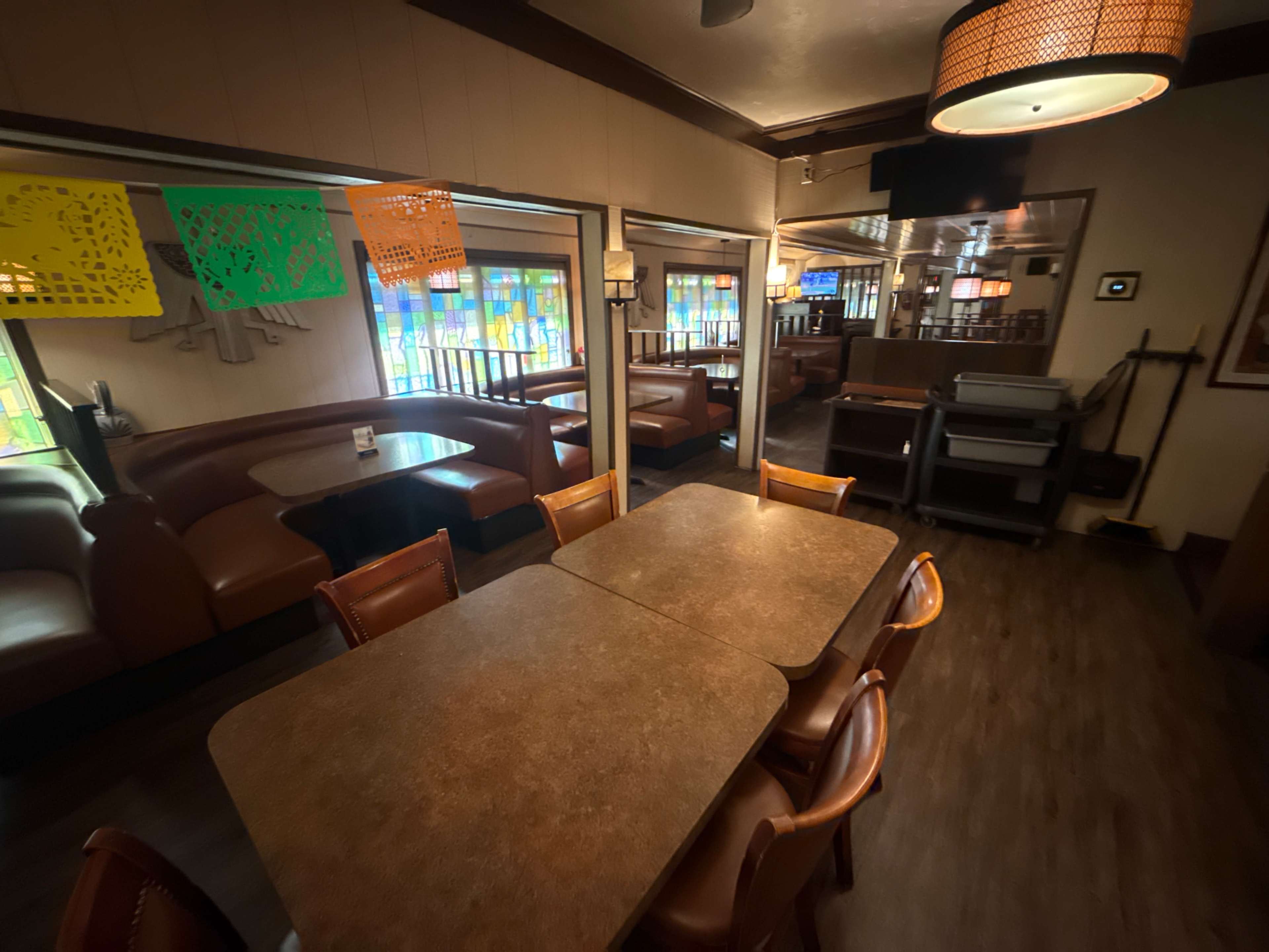 The image shows a neatly arranged dining area in a restaurant, featuring tables with brown surfaces and leather-seated booths, illuminated by decorative light fixtures.