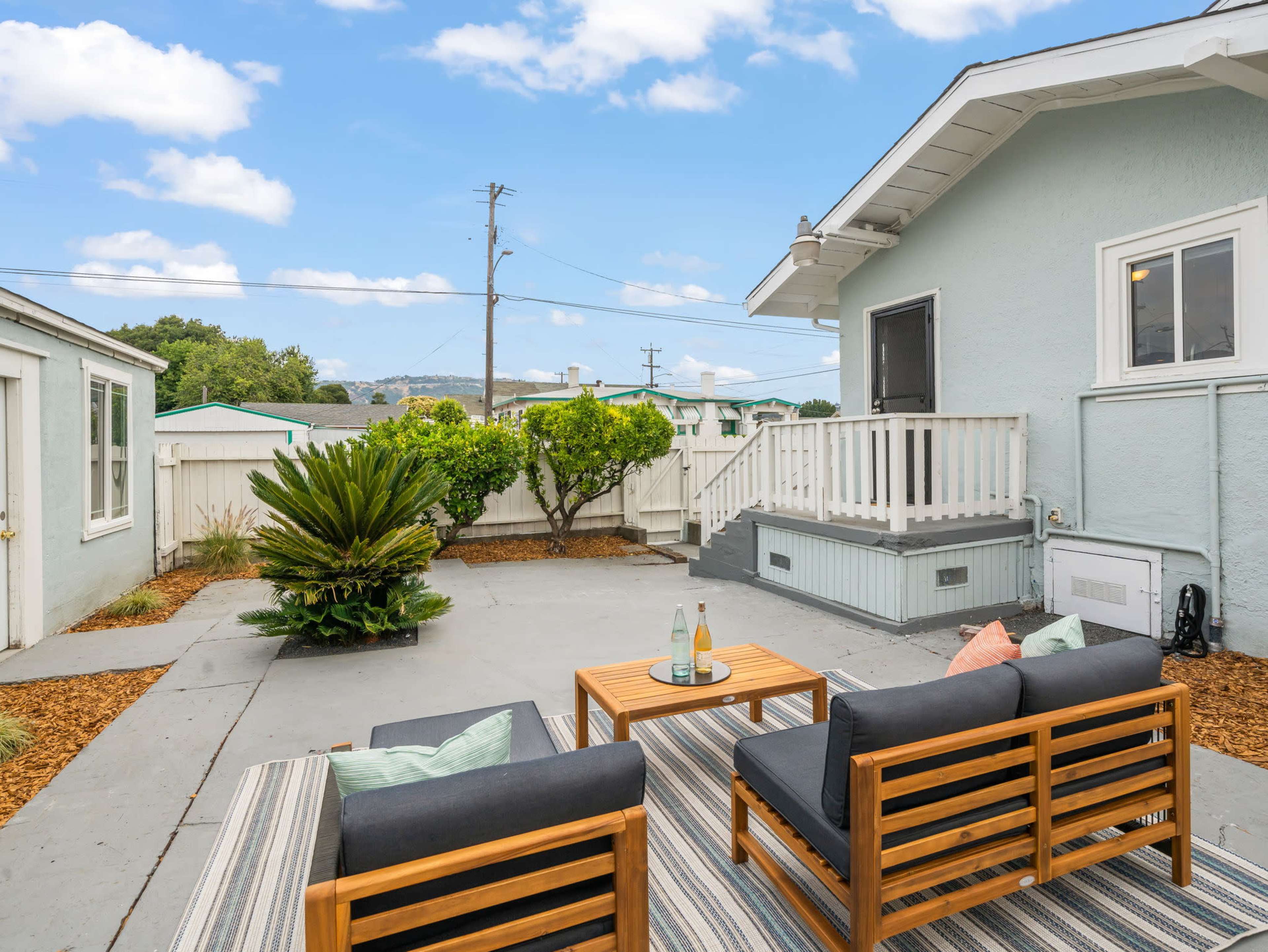 An outdoor seating area with two wooden chairs and a coffee table, surrounded by a small garden and a fenced yard.