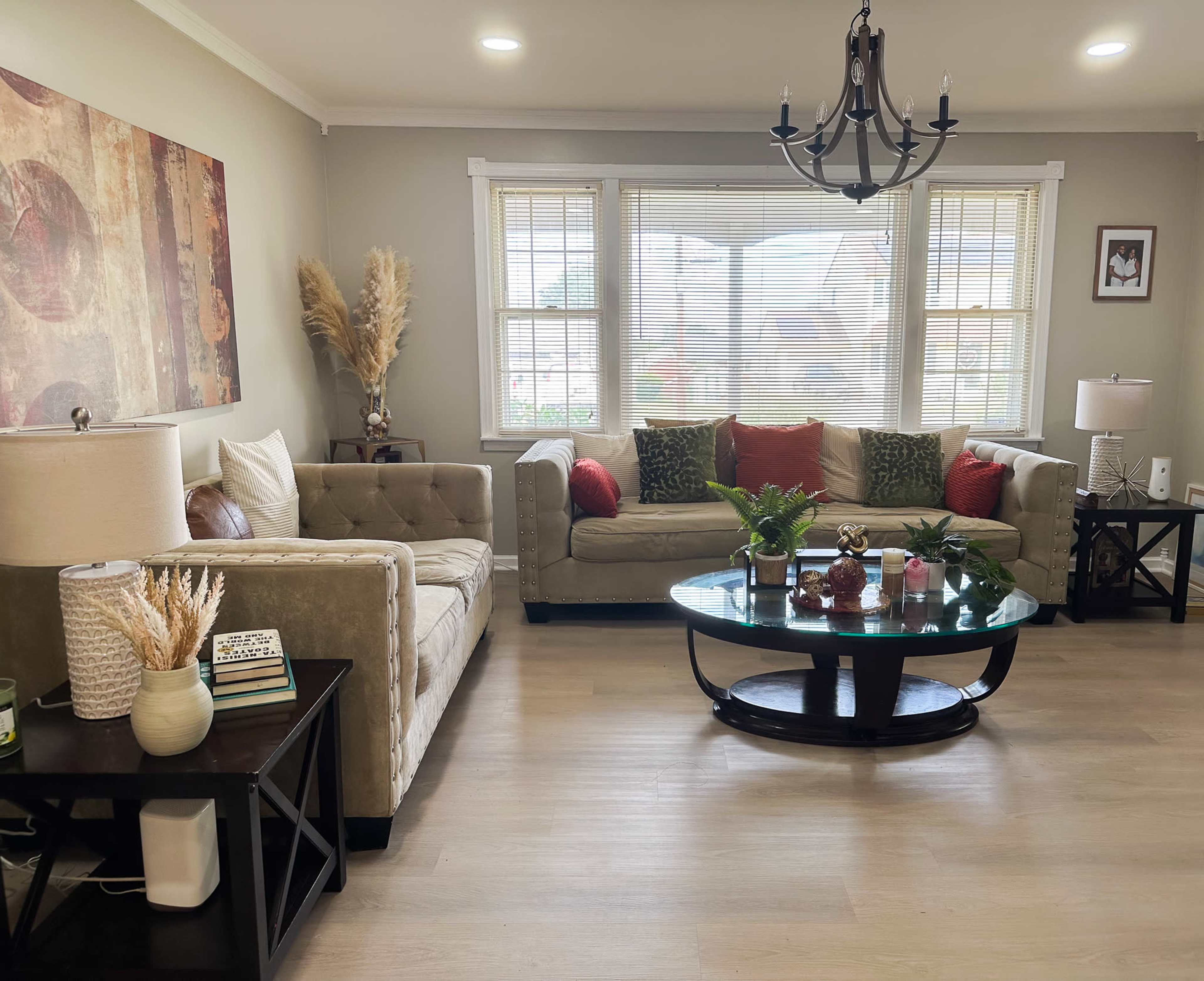 A cozy living room features a sectional sofa with decorative pillows, a round coffee table, and large windows allowing natural light to flood the space.