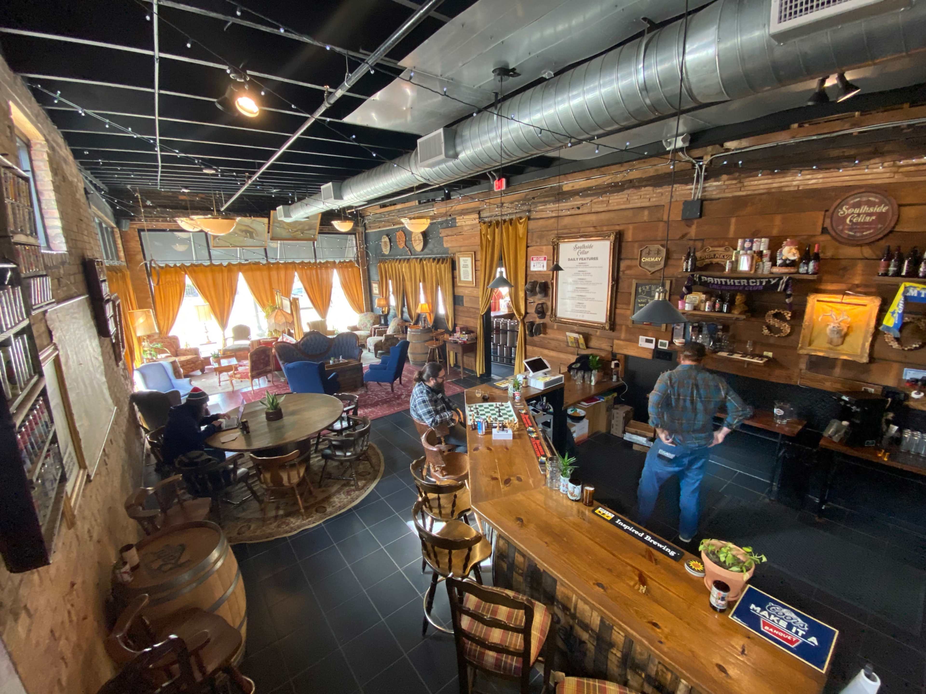 A cozy cafe with wooden decor, a central bar, and several seating areas illuminated by natural light.