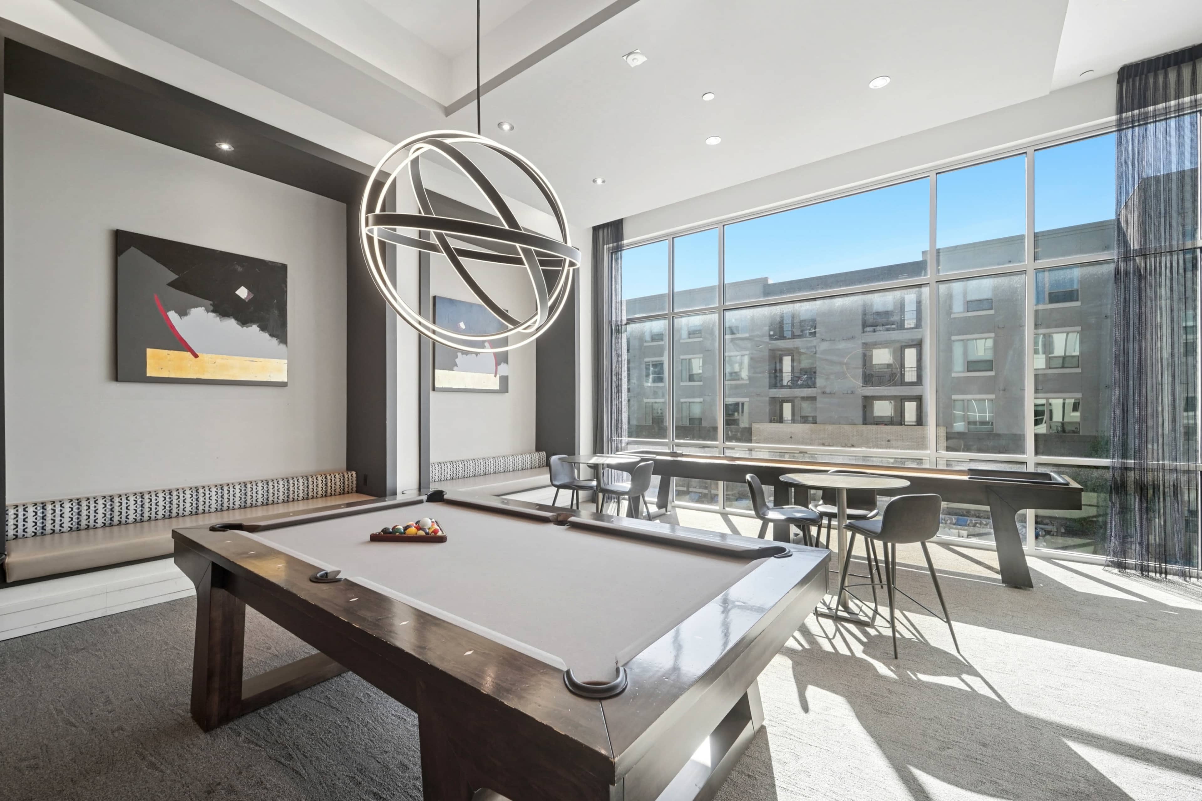 A modern game room features a pool table, contemporary lighting, and large windows overlooking an outdoor area.