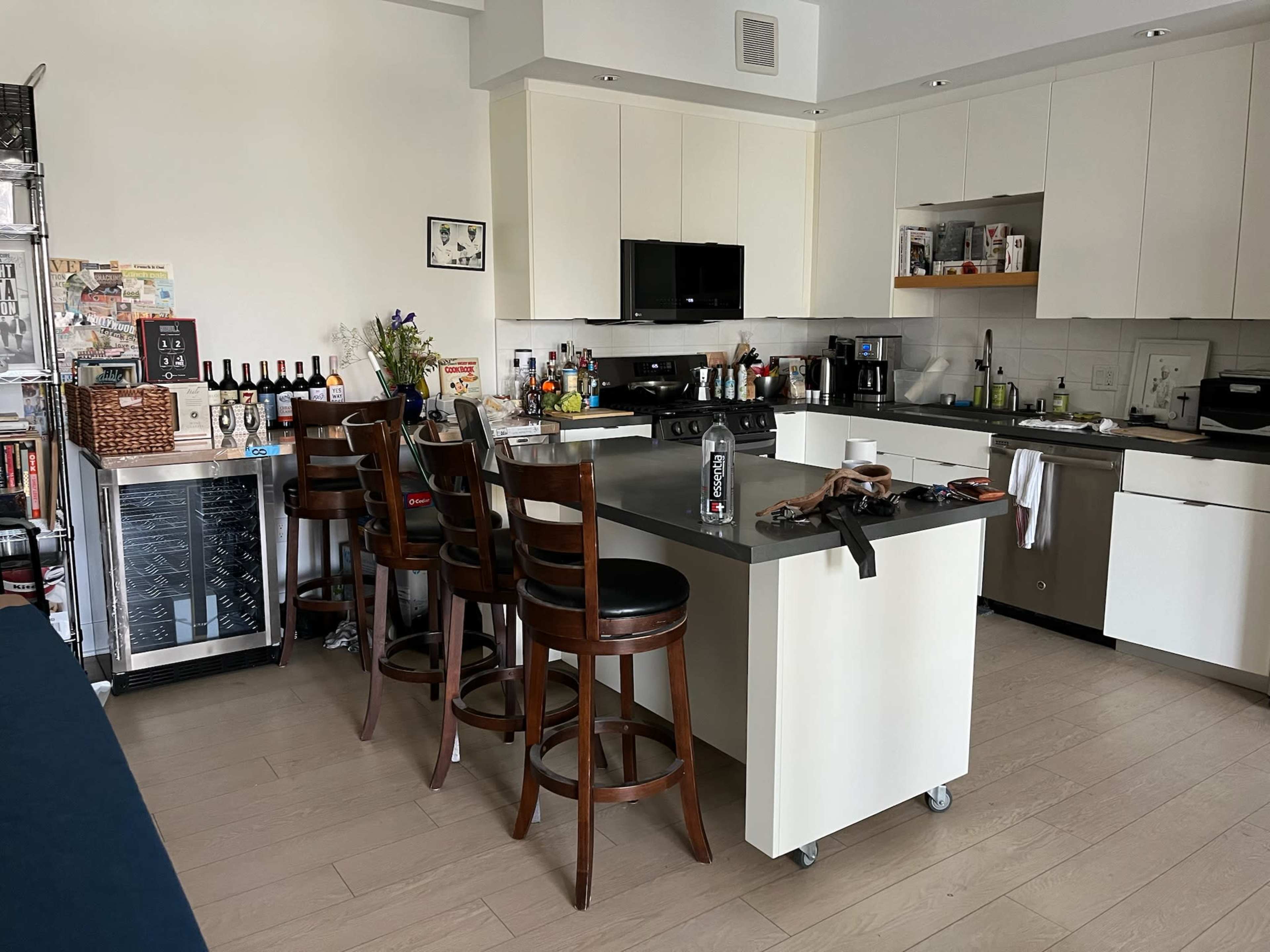 The image shows a modern kitchen with a central island, bar stools, and various appliances and items on countertops.