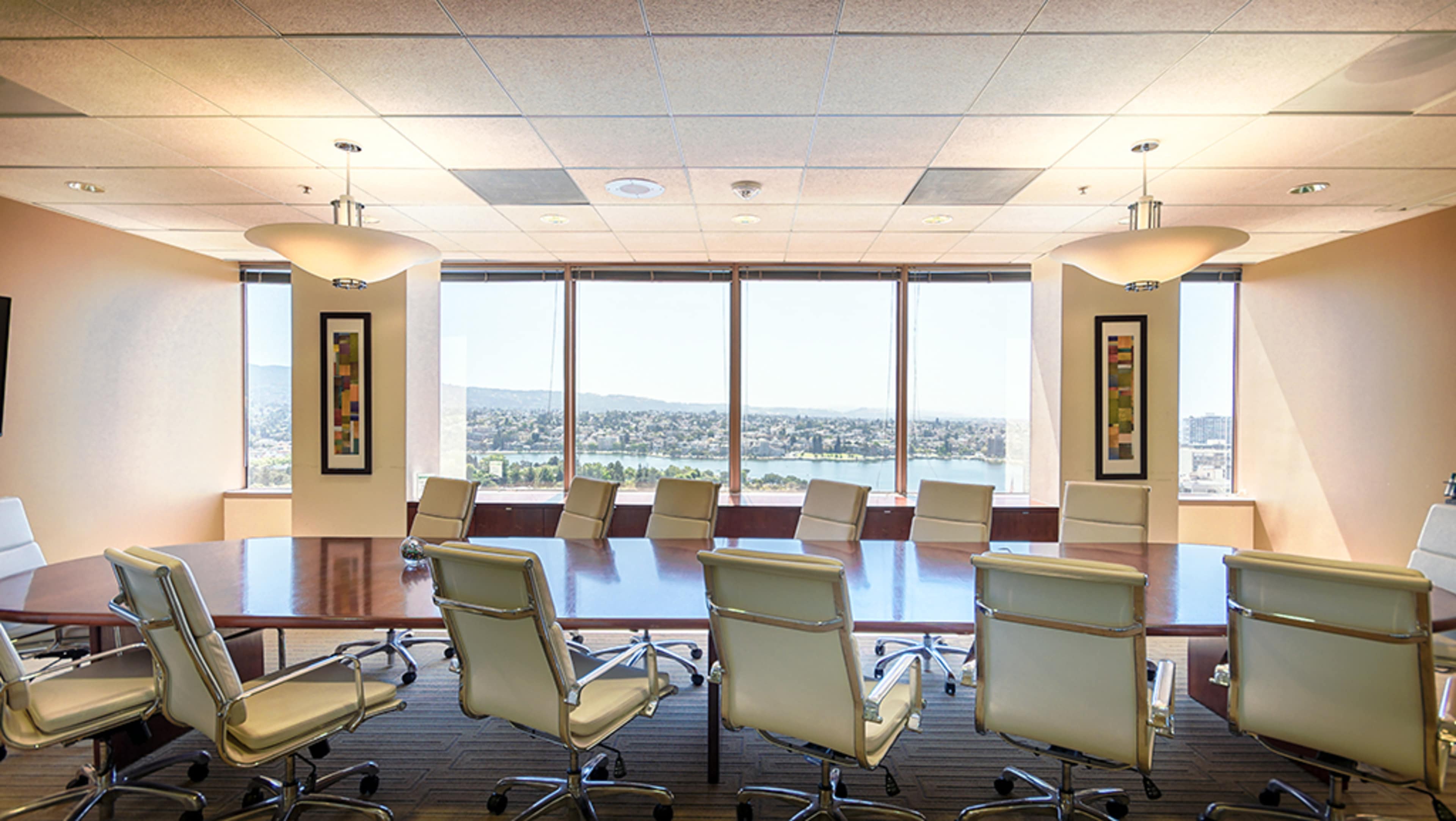 A large conference room features a long table surrounded by white chairs, with large windows providing a view of the city and mountains in the distance.