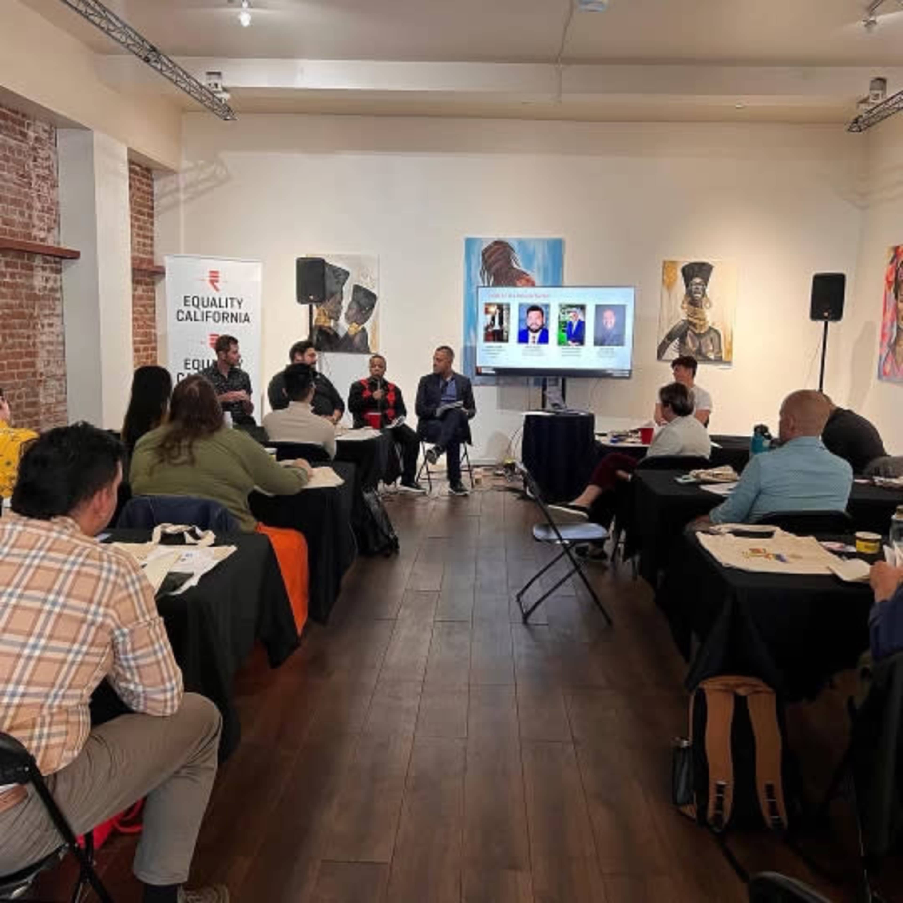A group of people is attending a panel discussion in a room with exposed brick walls and artwork on display.