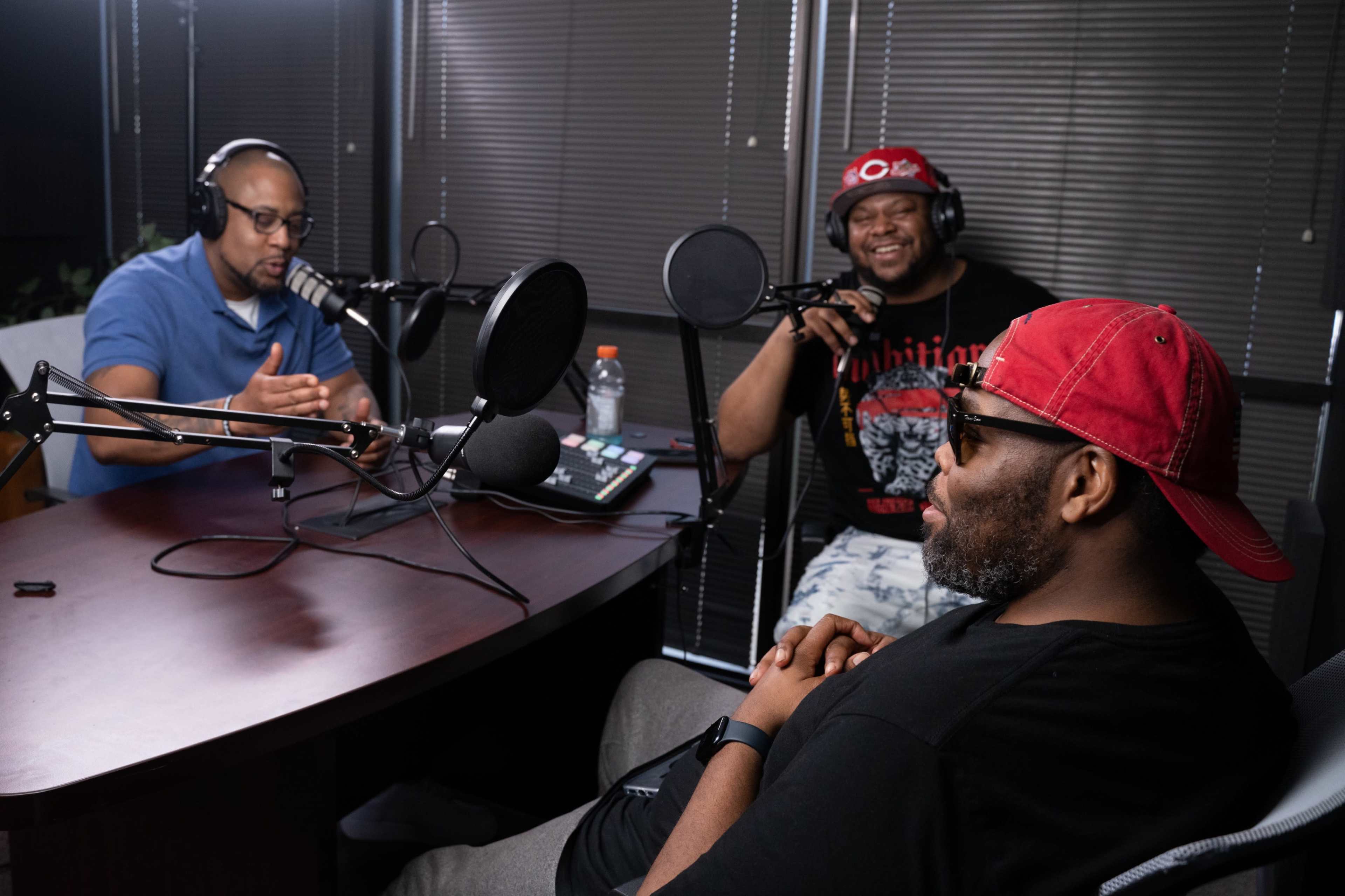 Three men are engaged in a podcast discussion at a table with microphones and recording equipment.