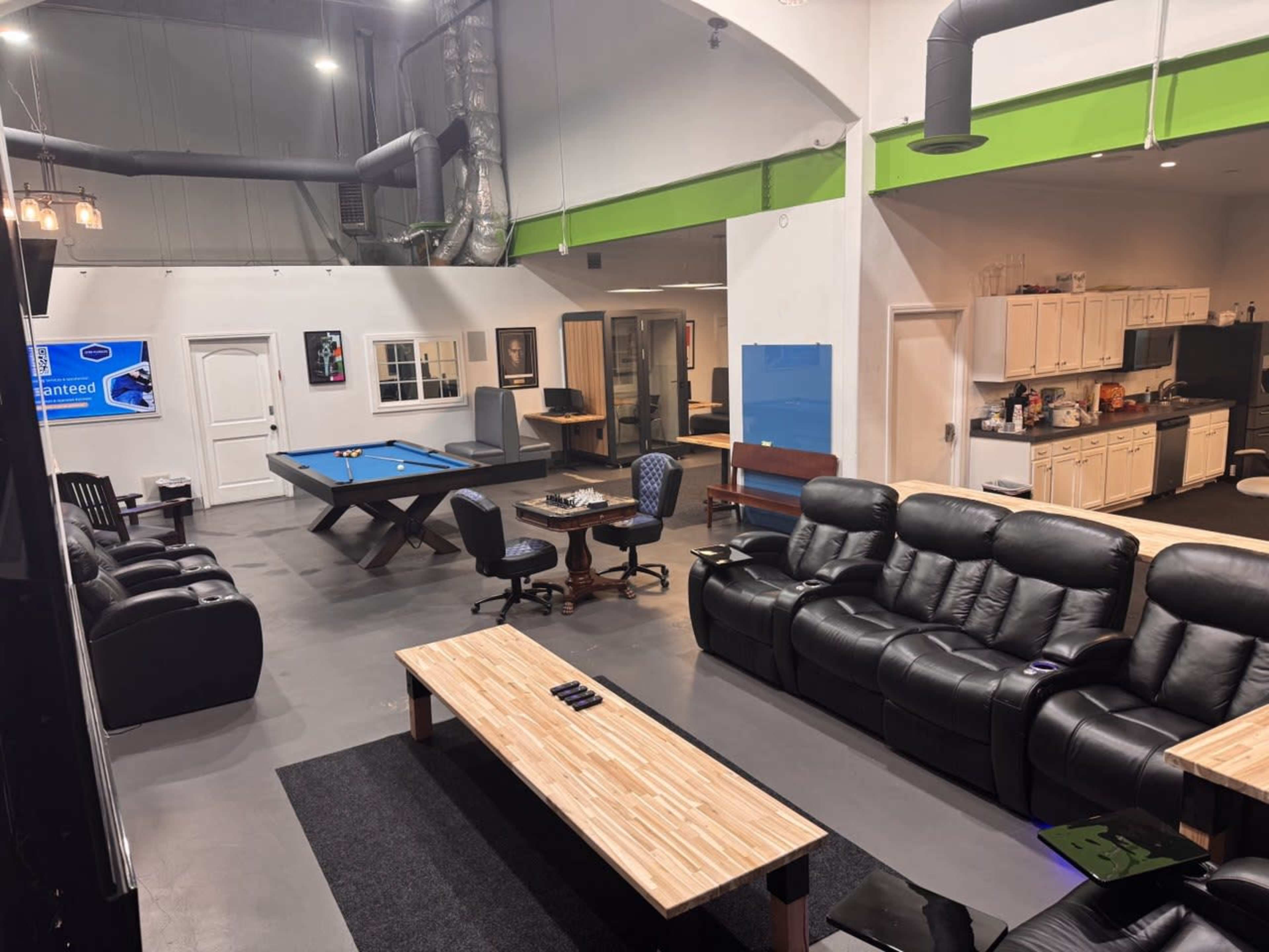 The image shows a spacious room with seating areas, a pool table, a kitchenette, and various workstations.