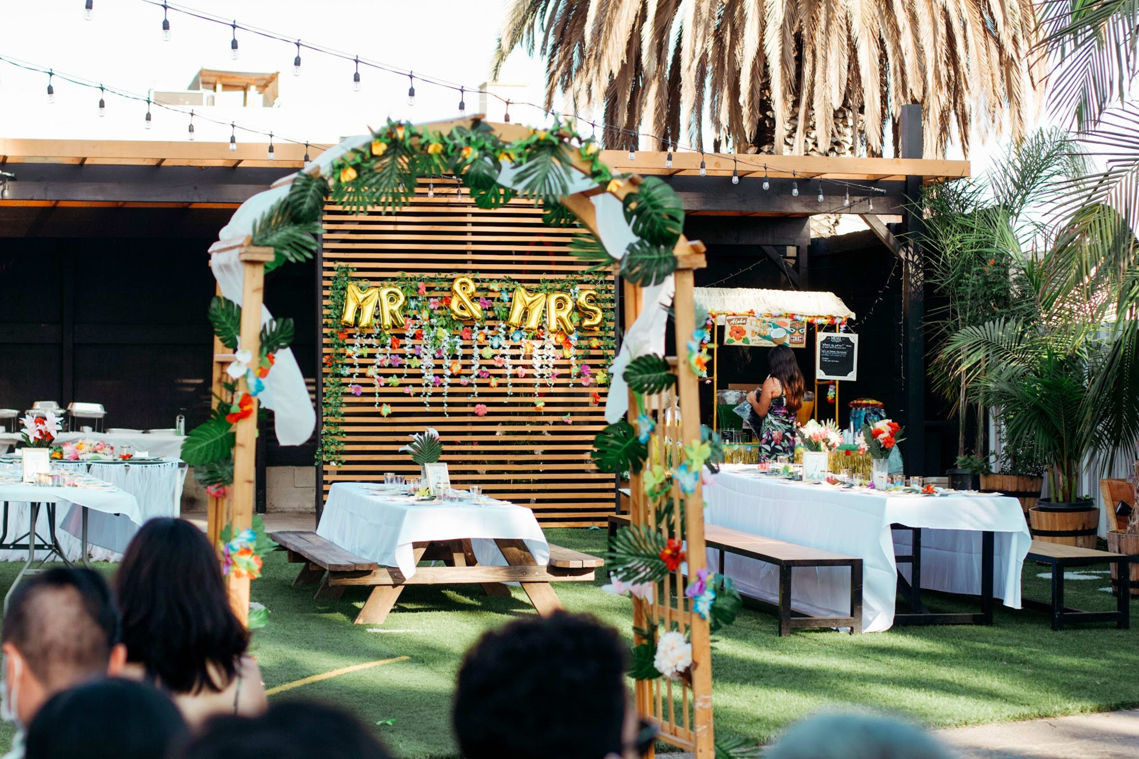 A group of people sitting outside near picnic tables for a tiki-themed wedding celebration.