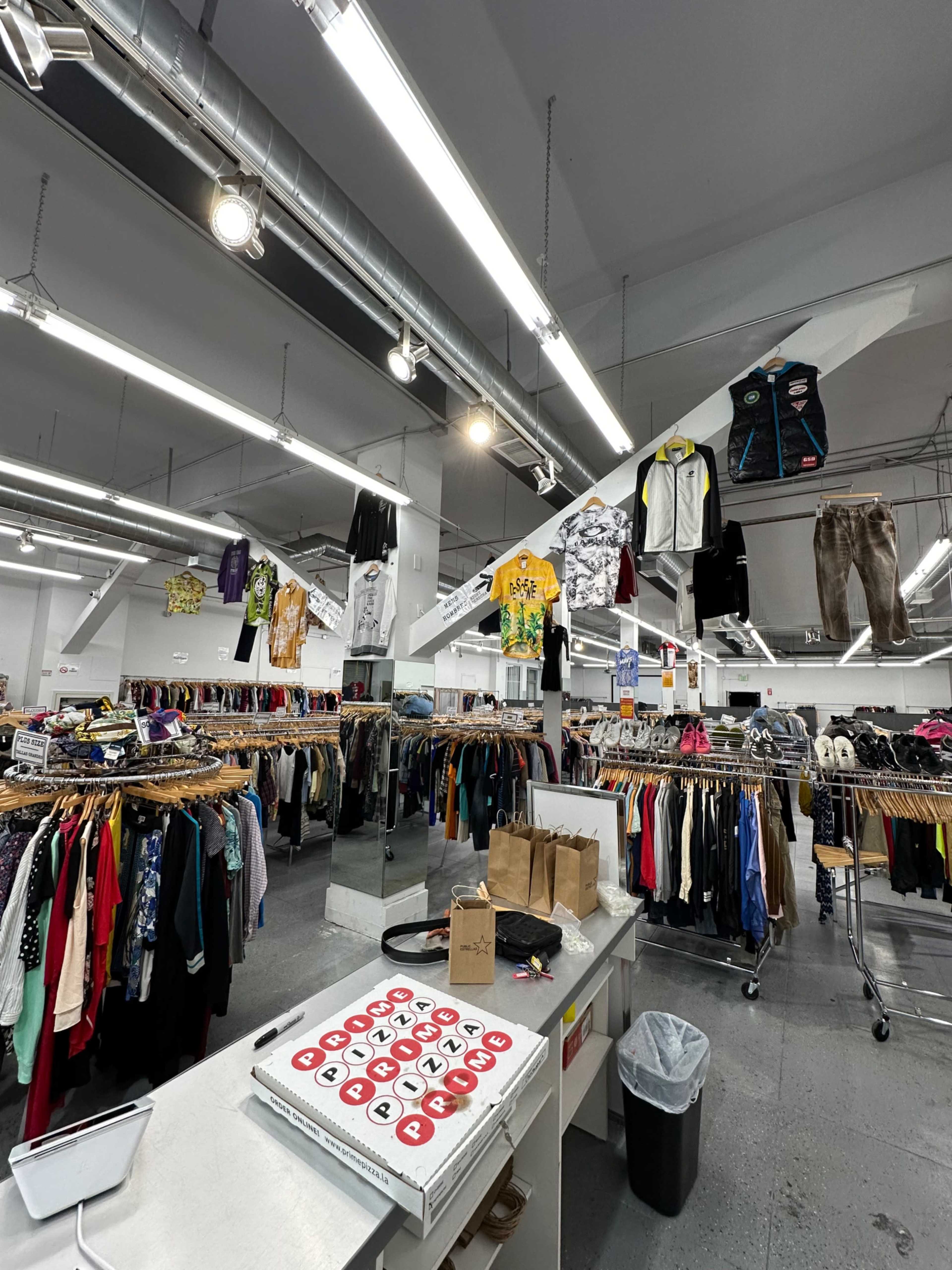 The image shows the interior of a thrift store with racks of clothing and various garments hanging from the ceiling.