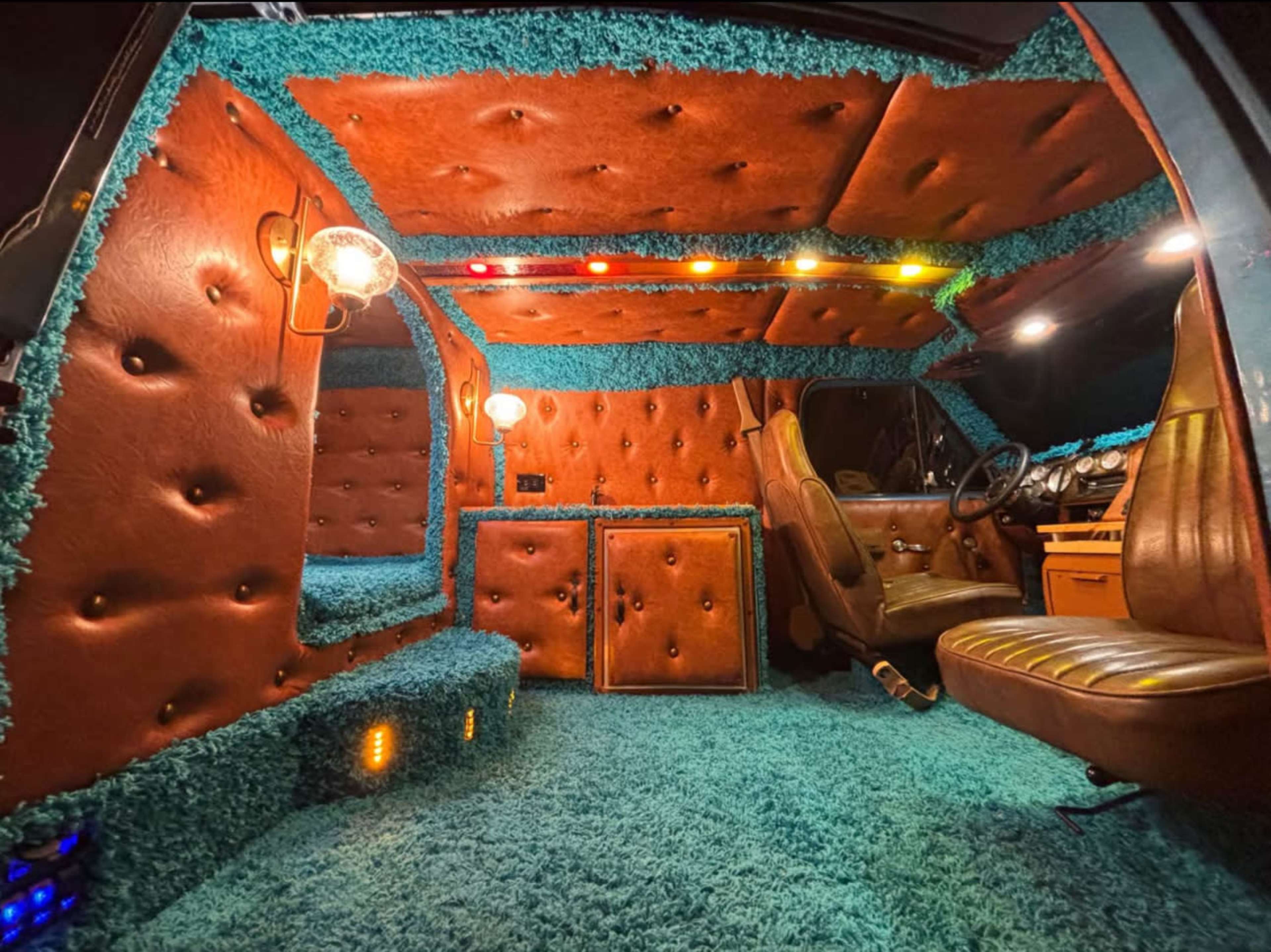 The interior of the car features plush, tufted leather on the walls and seats, with vibrant blue carpeting and colorful lighting.