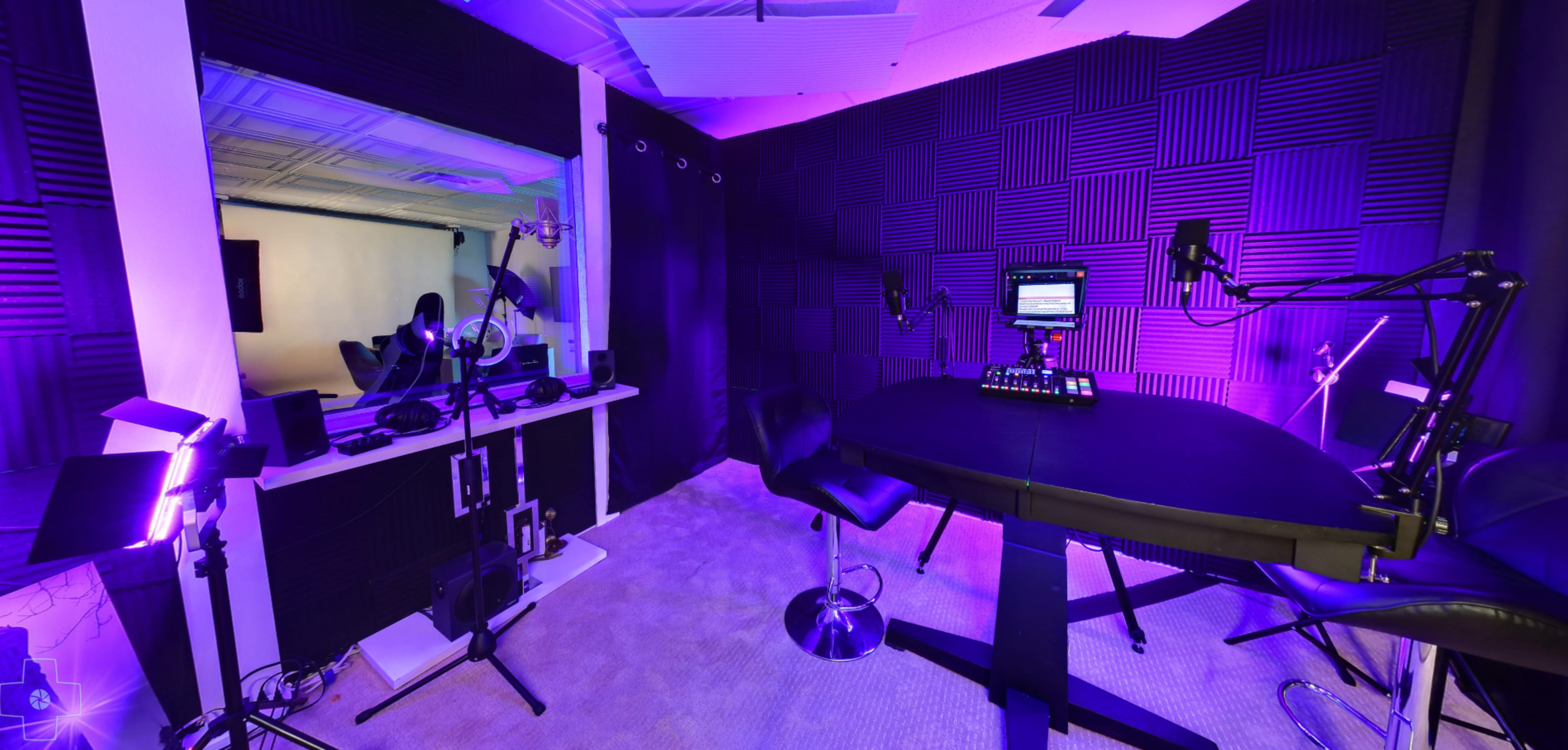 A modern recording studio with padded walls, a central round table, adjustable microphone stands, and lighting equipment.