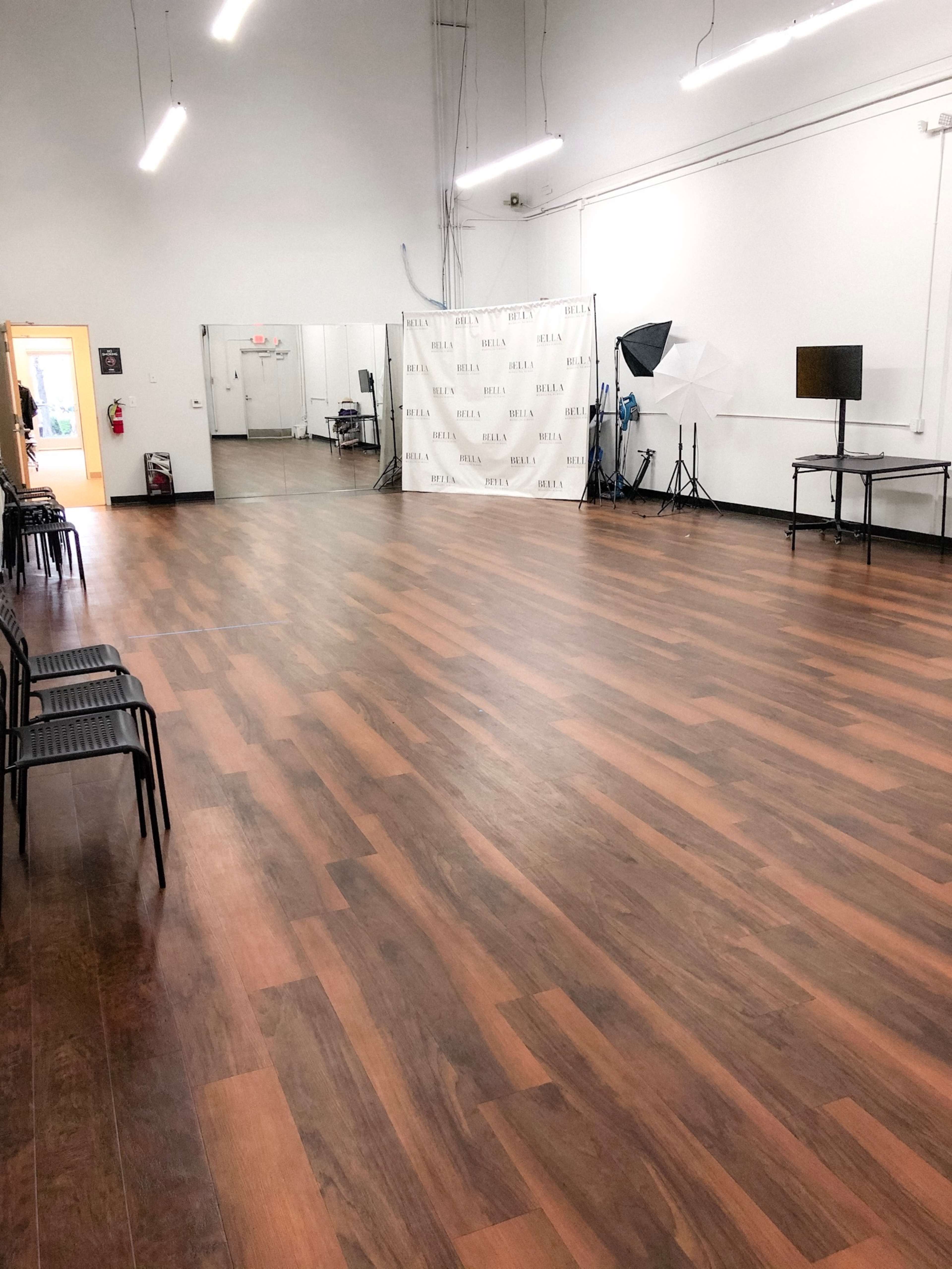 A spacious, empty dance studio with wooden floors, a mirrored wall, and various lighting equipment set up in the corner.