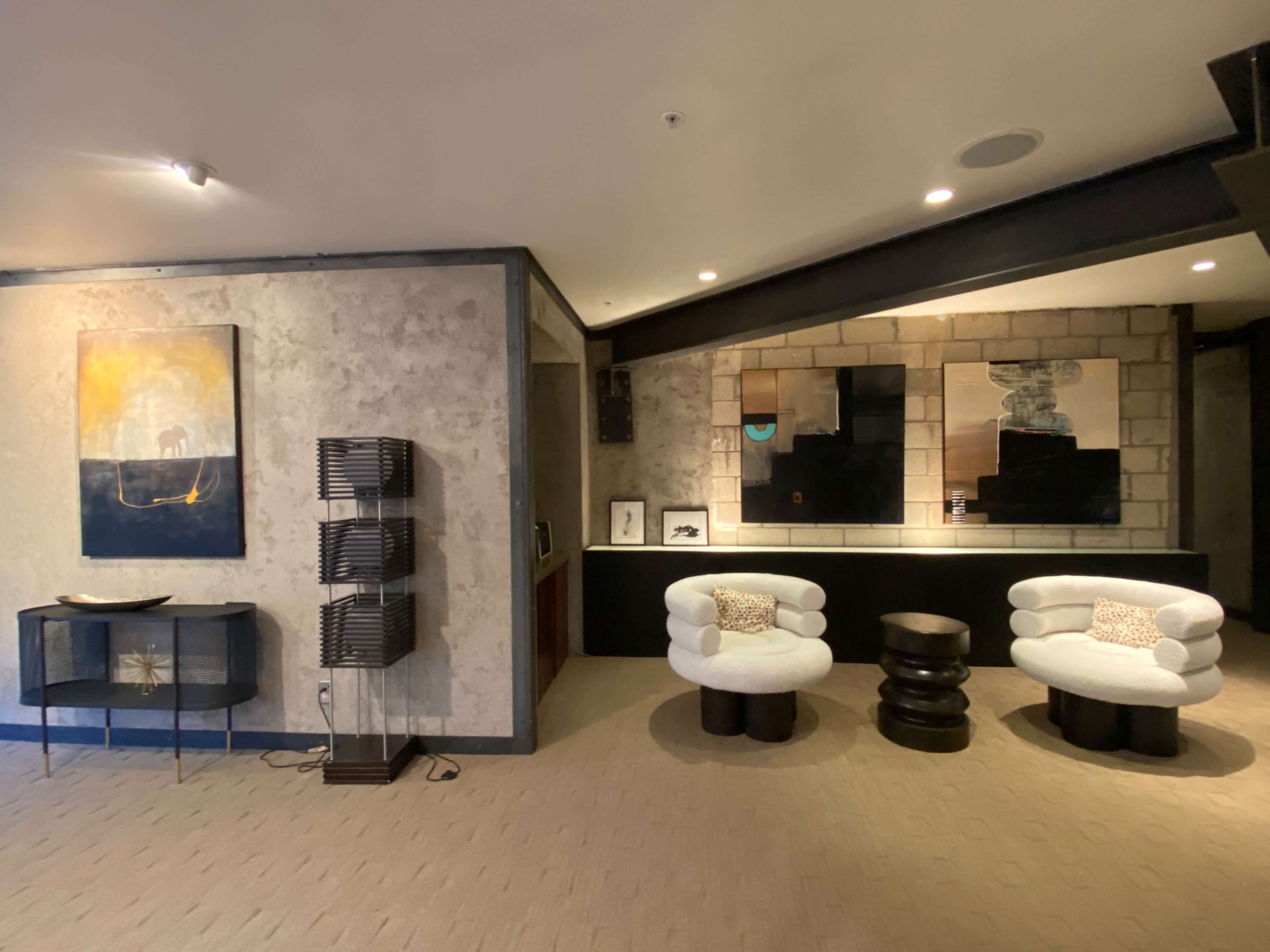 A modern lounge area with two tufted chairs, a black end table, a decorative console table, and a large artwork on the wall.