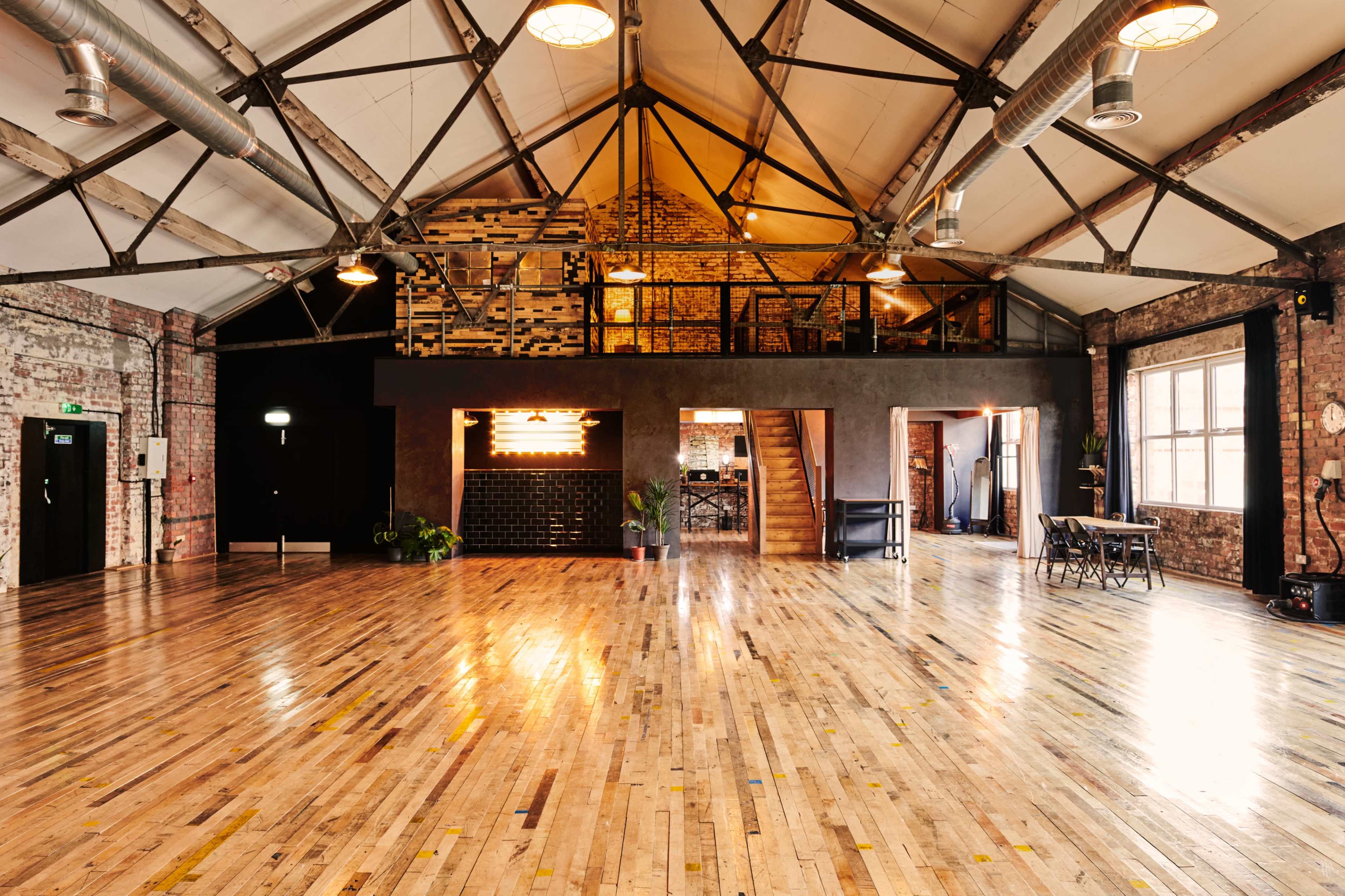 An industrial-style event space with high ceilings, exposed brick walls, and polished wooden floors.