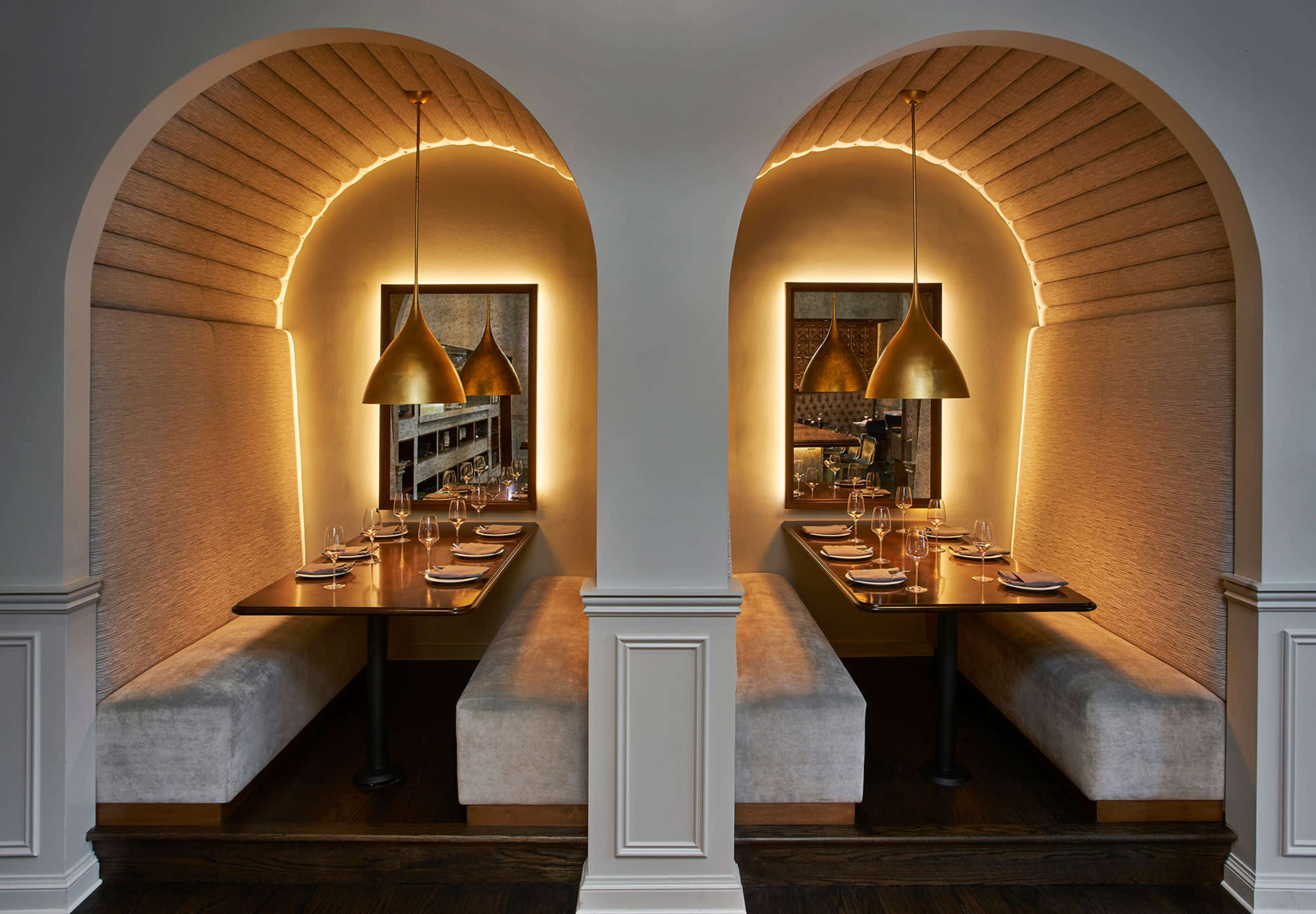 The image shows two cozy dining alcoves with curved archways, each featuring a table set for dinner under warm pendant lights.