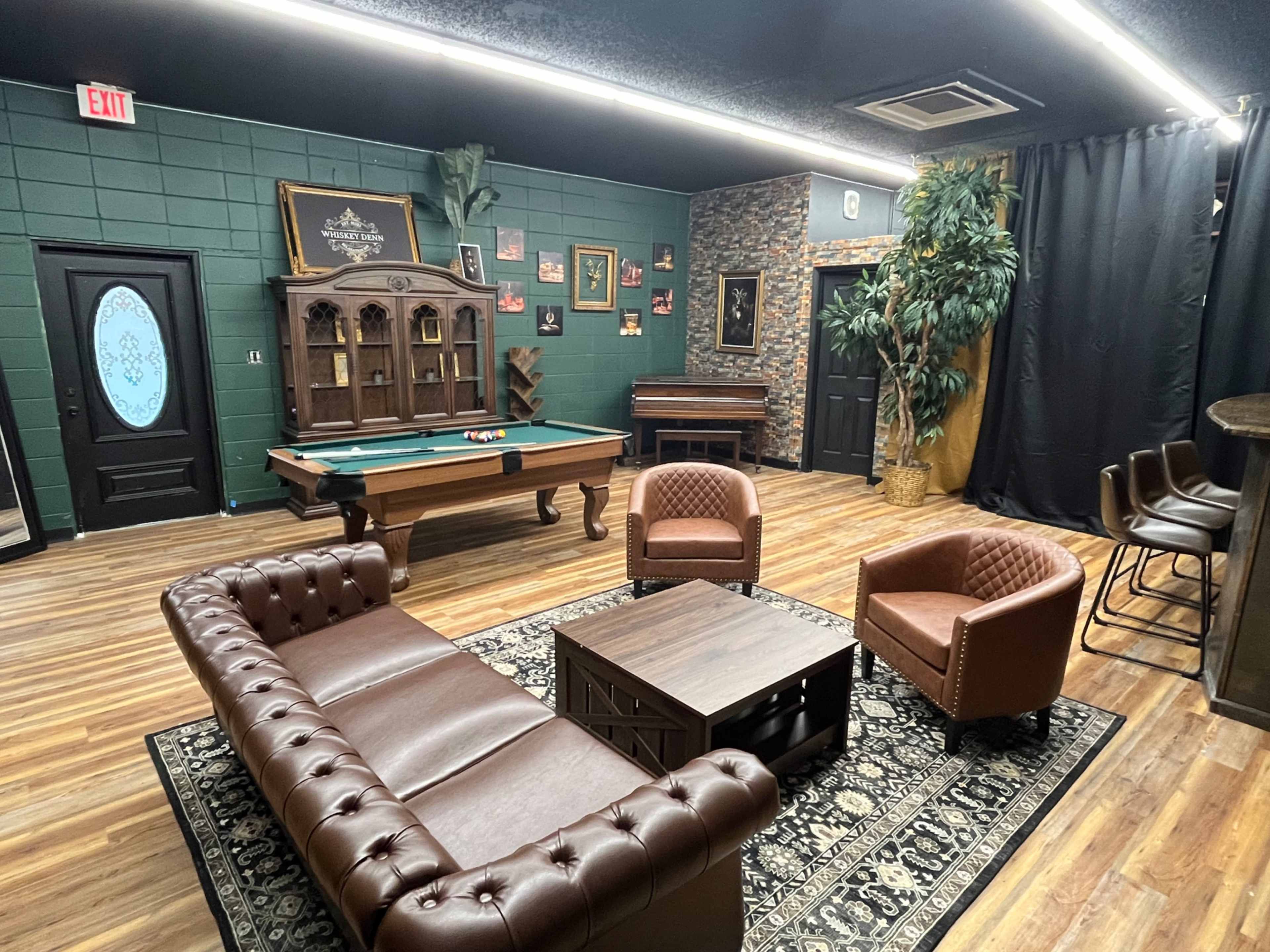 The image shows a game room with a pool table, a seating area featuring a brown leather sofa and armchairs, and decor that includes a piano and various framed pictures on the walls.