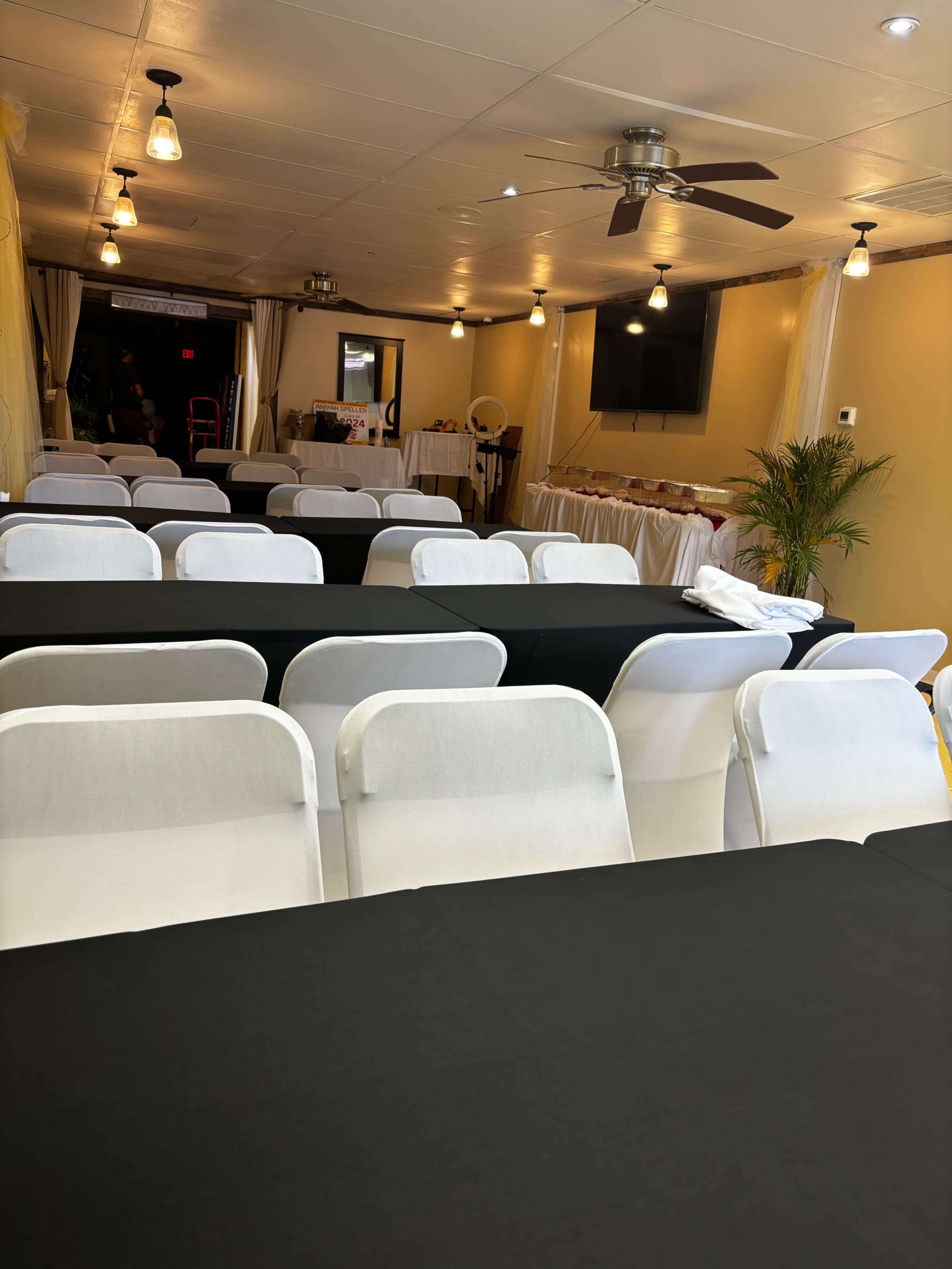 The image shows a banquet hall with rows of tables covered in black and white tablecloths, set up for an event.