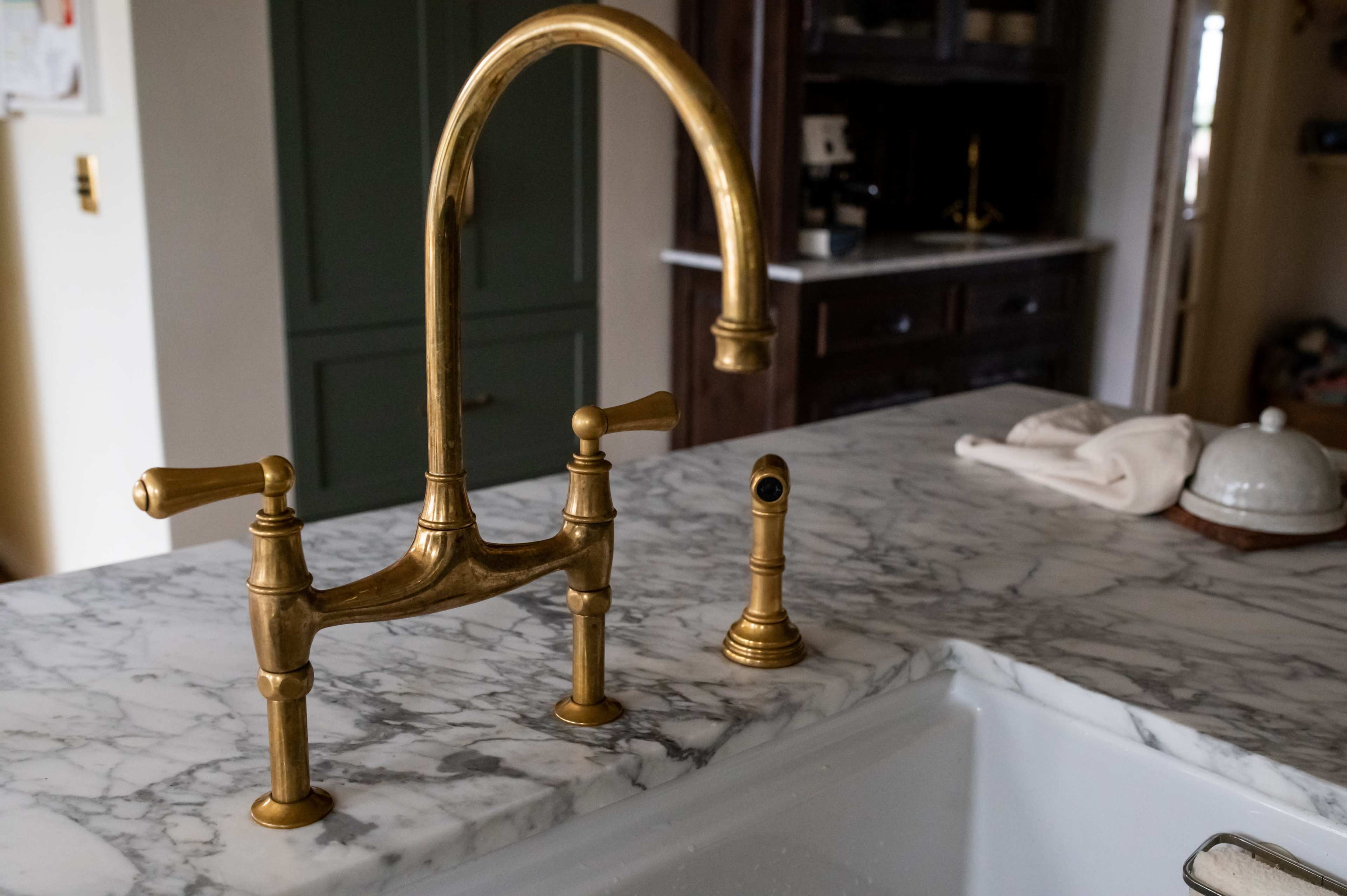 The image shows a brass kitchen faucet installed on a marble countertop.