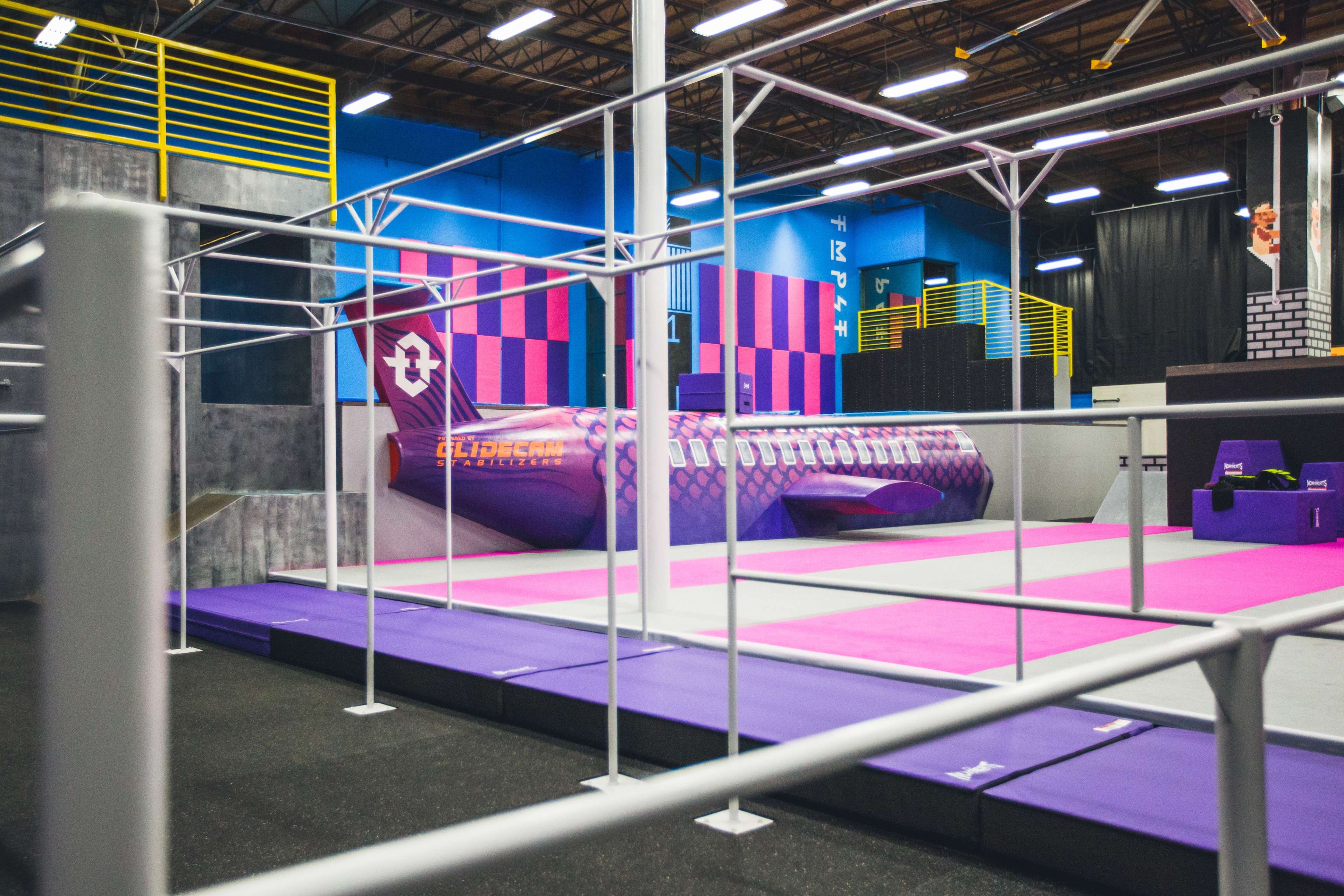 A colorful indoor trampoline park featuring a large, stylized airplane structure surrounded by various colored mats.