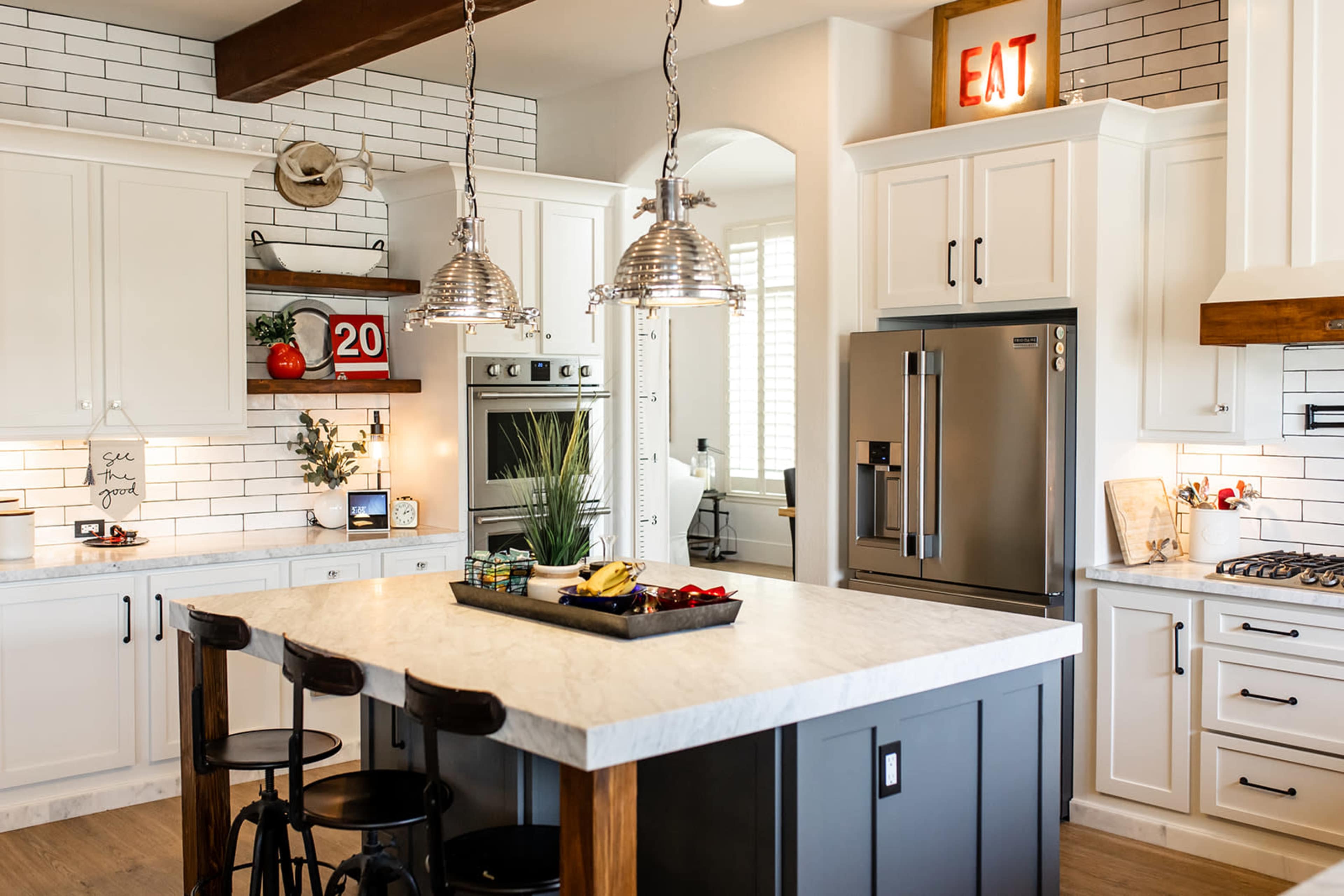 The image shows a modern kitchen with white cabinets, a large island featuring a marble countertop, and industrial-style pendant lights hanging above.