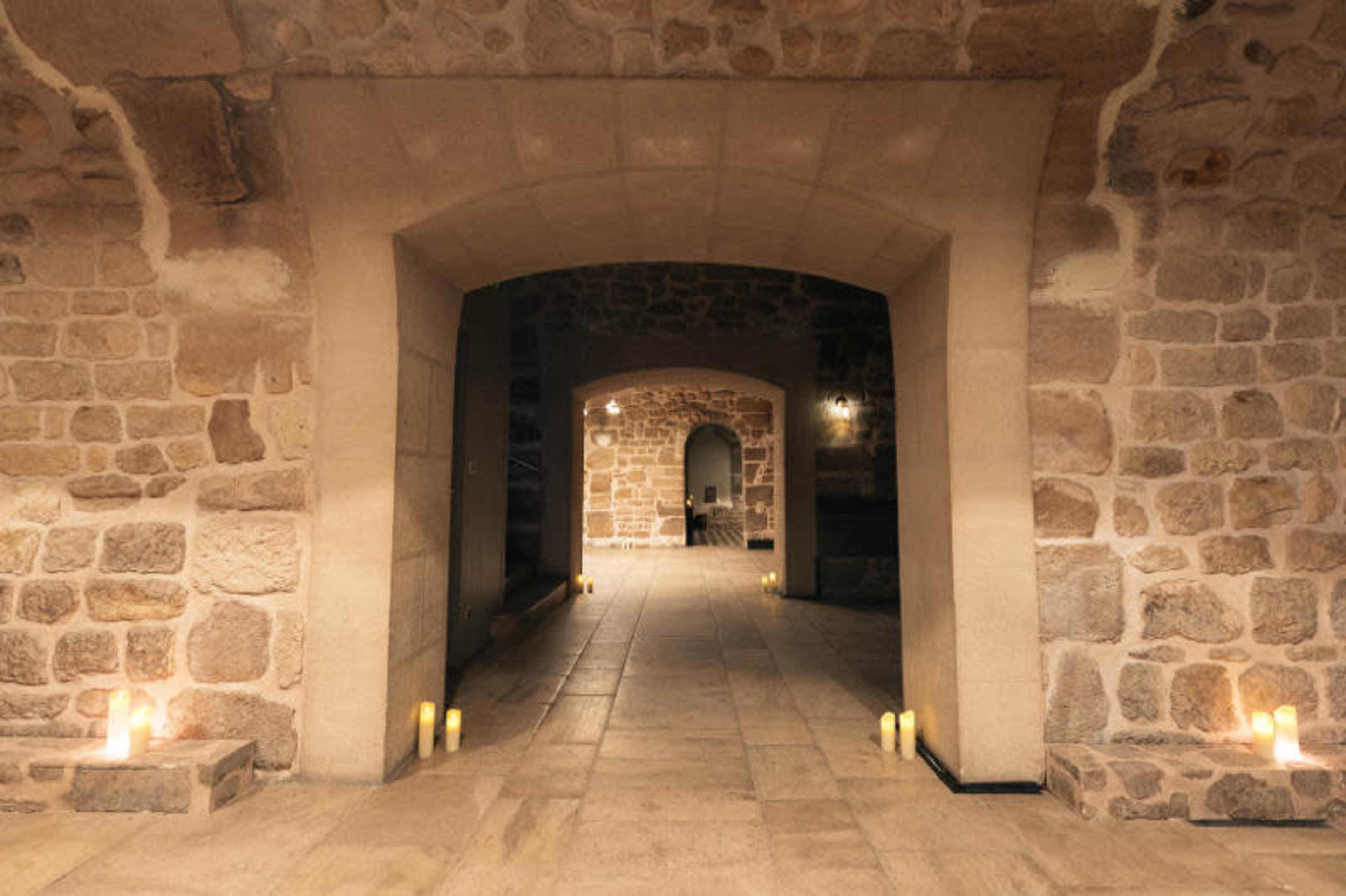 The image shows a stone-walled interior space with multiple archways and candles lining the floor.