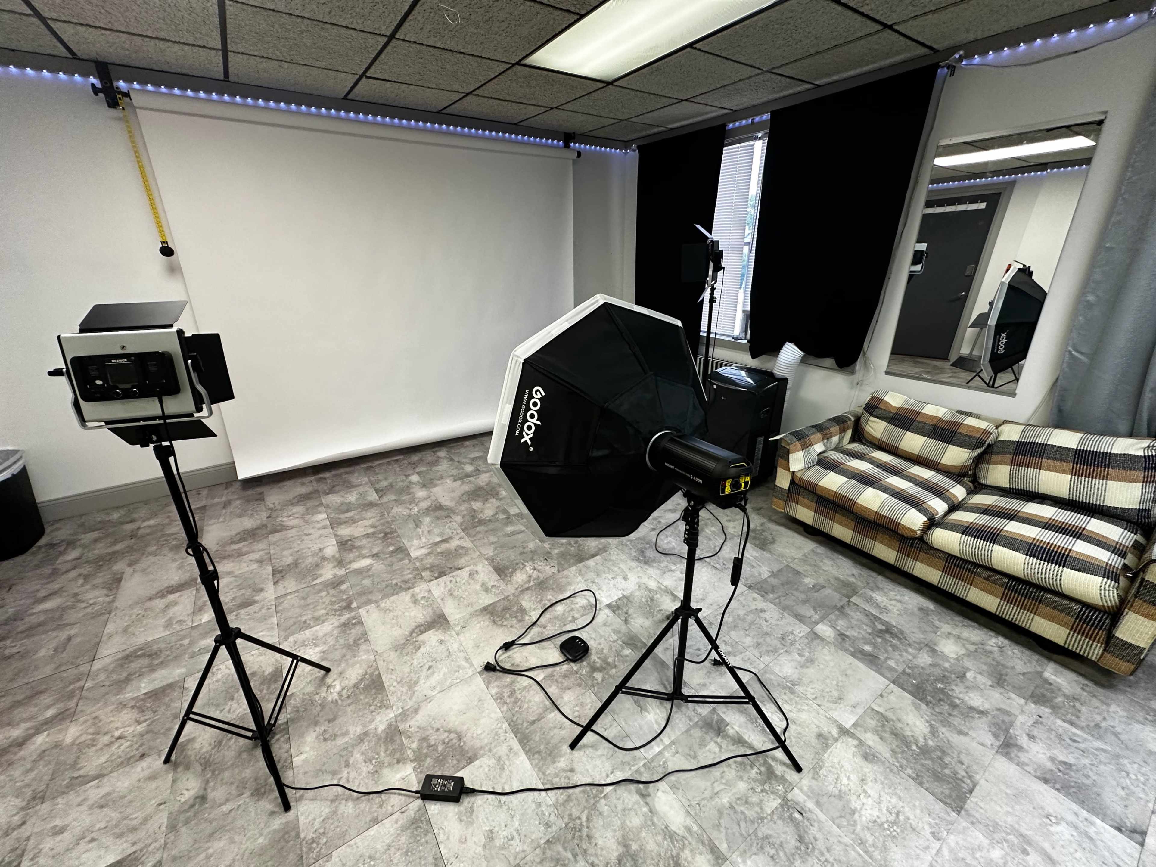 A photography studio setup with a backdrop, lighting equipment, and a couch in a corner.
