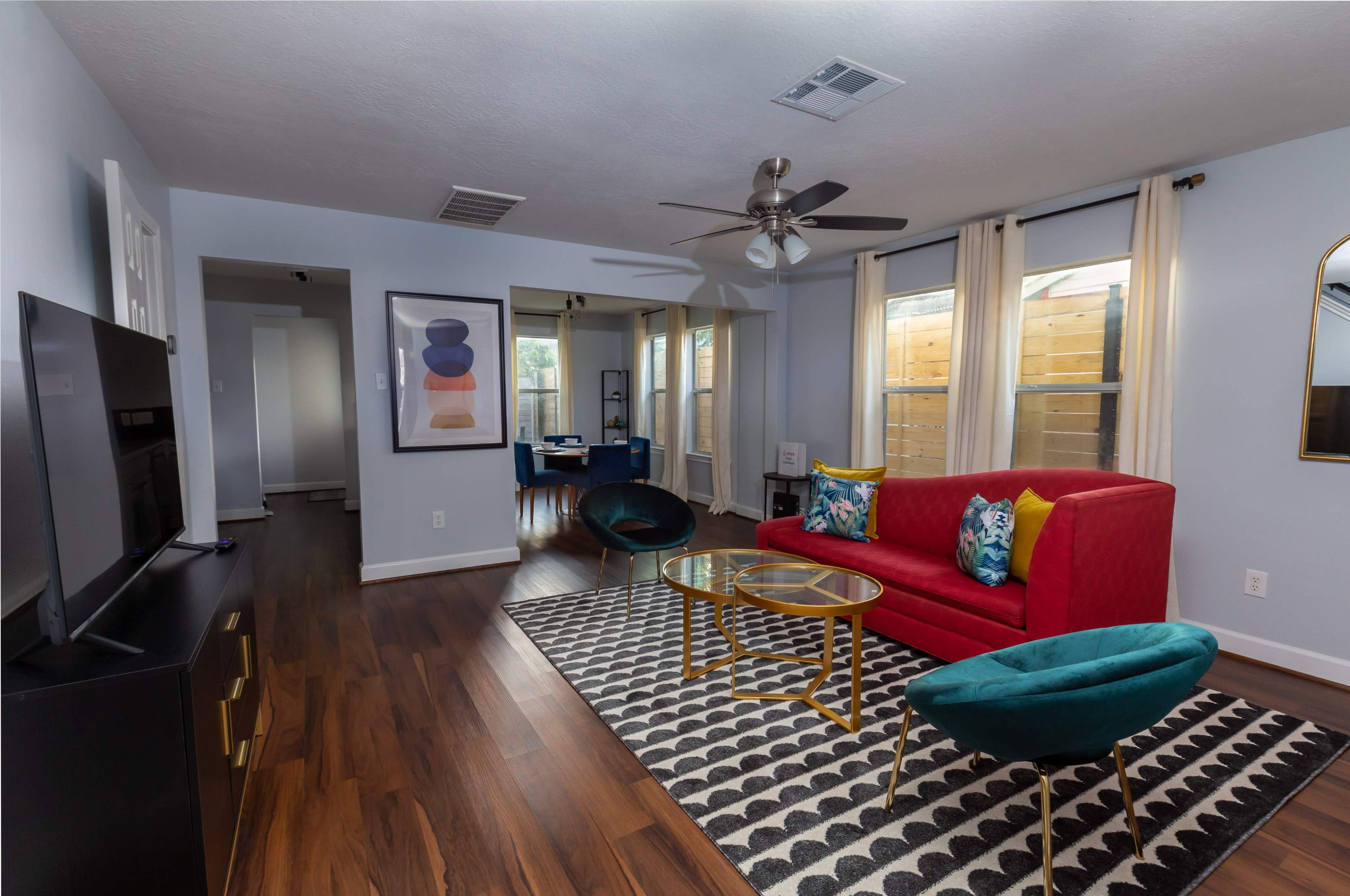 The living room features a red sofa, a patterned area rug, a television on a black stand, and a view of a small outdoor area through large windows.