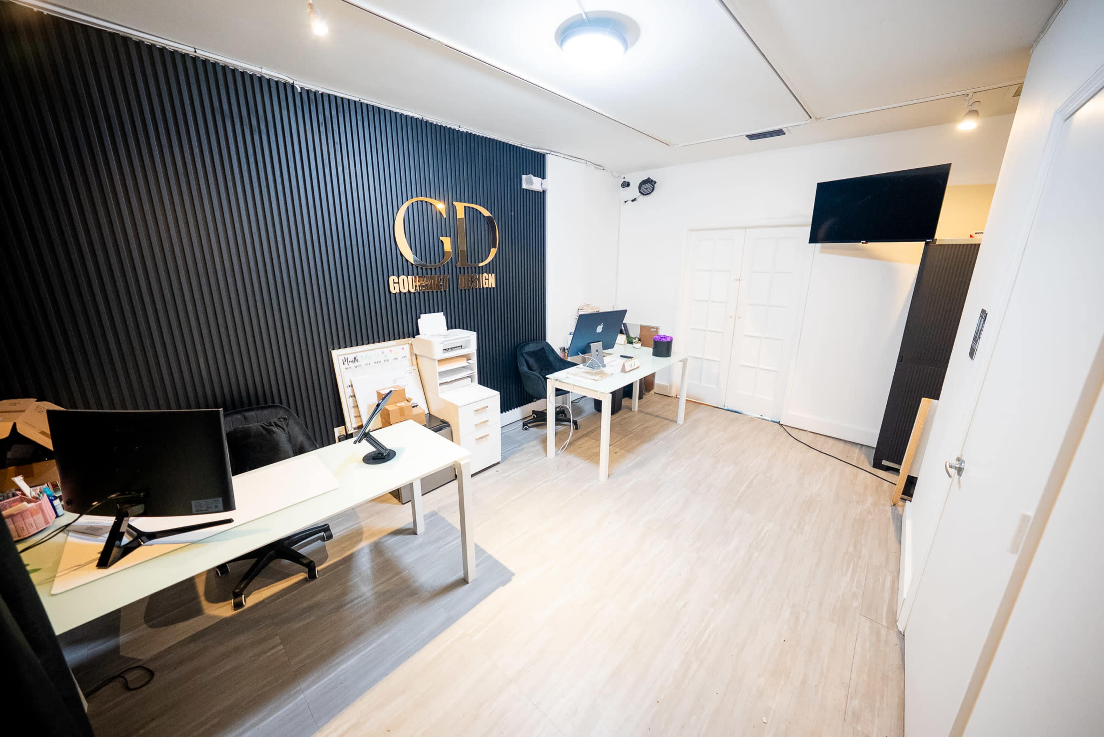 An office space features two desks with computers, a television mounted on the wall, and a modern design with a sleek black and white color scheme.