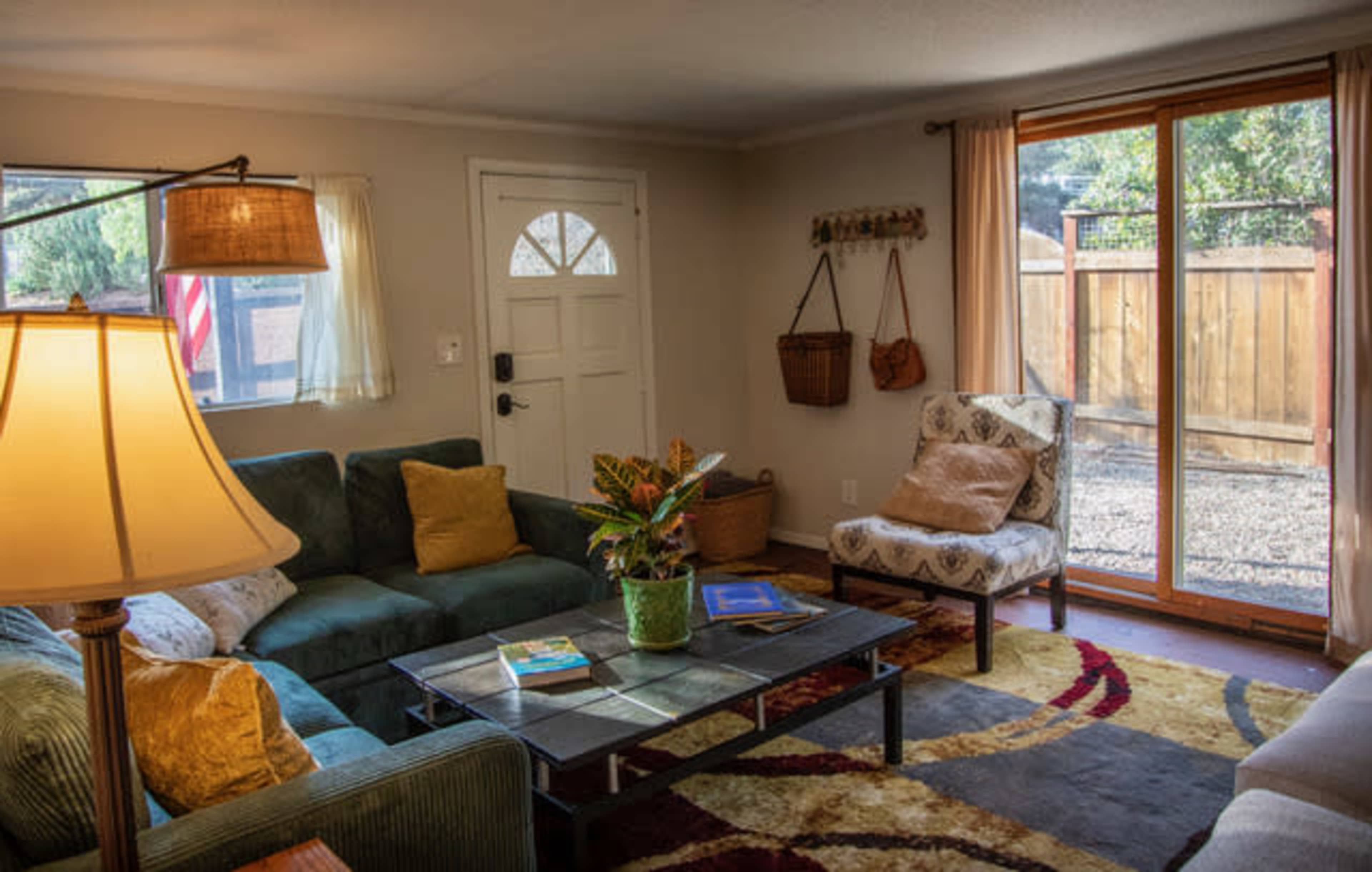 The image shows a cozy living room featuring a green sofa, an armchair, a coffee table, and a door leading to an outdoor area.