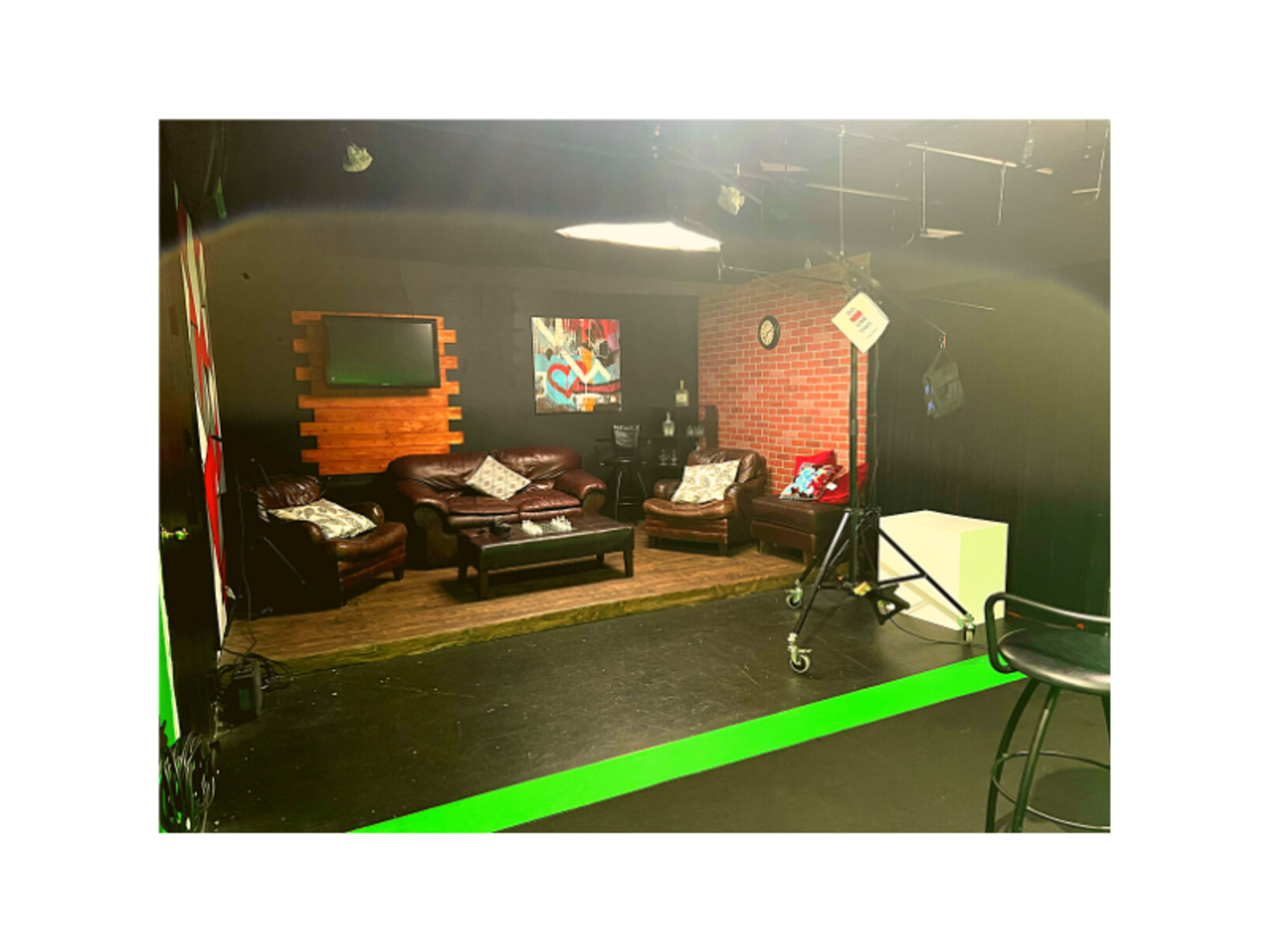 A television studio set featuring leather sofas, a wooden floor, and various backdrop elements including a brick wall and a clock.