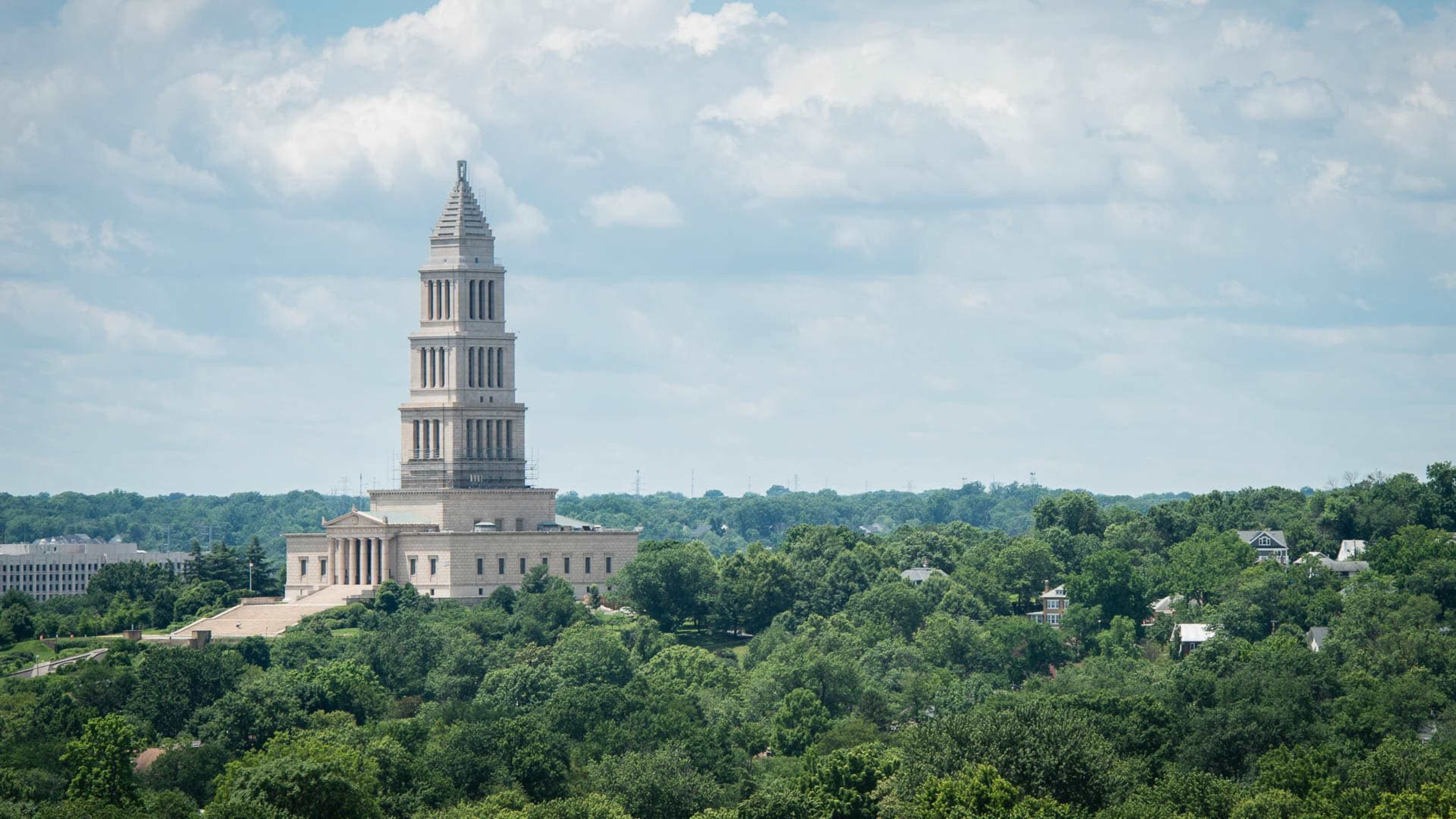 A tall stone tower surrounded by lush green trees under a partly cloudy sky.