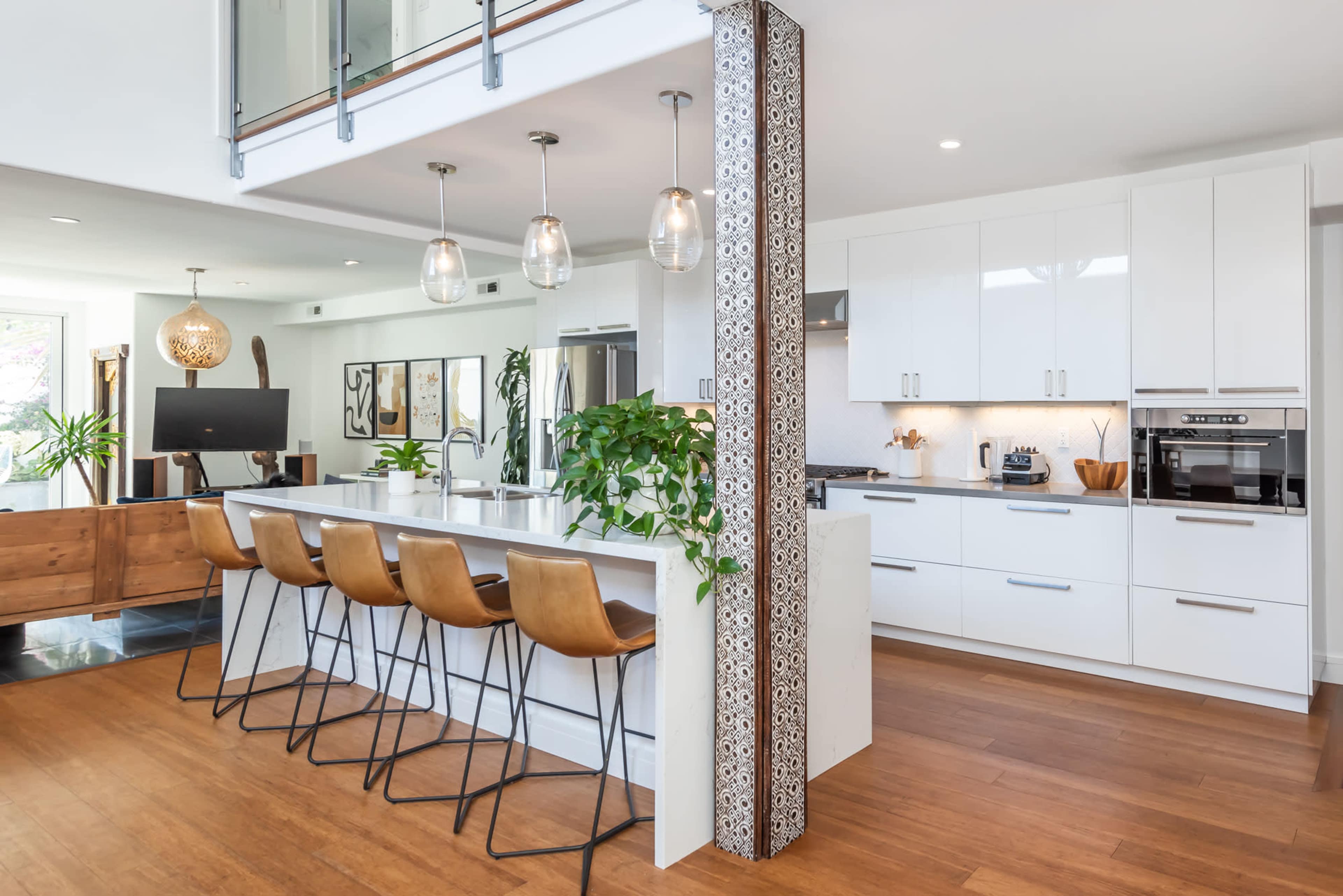 A modern kitchen with a white cabinetry, a central island with bar stools, and large windows that allow natural light to fill the space.