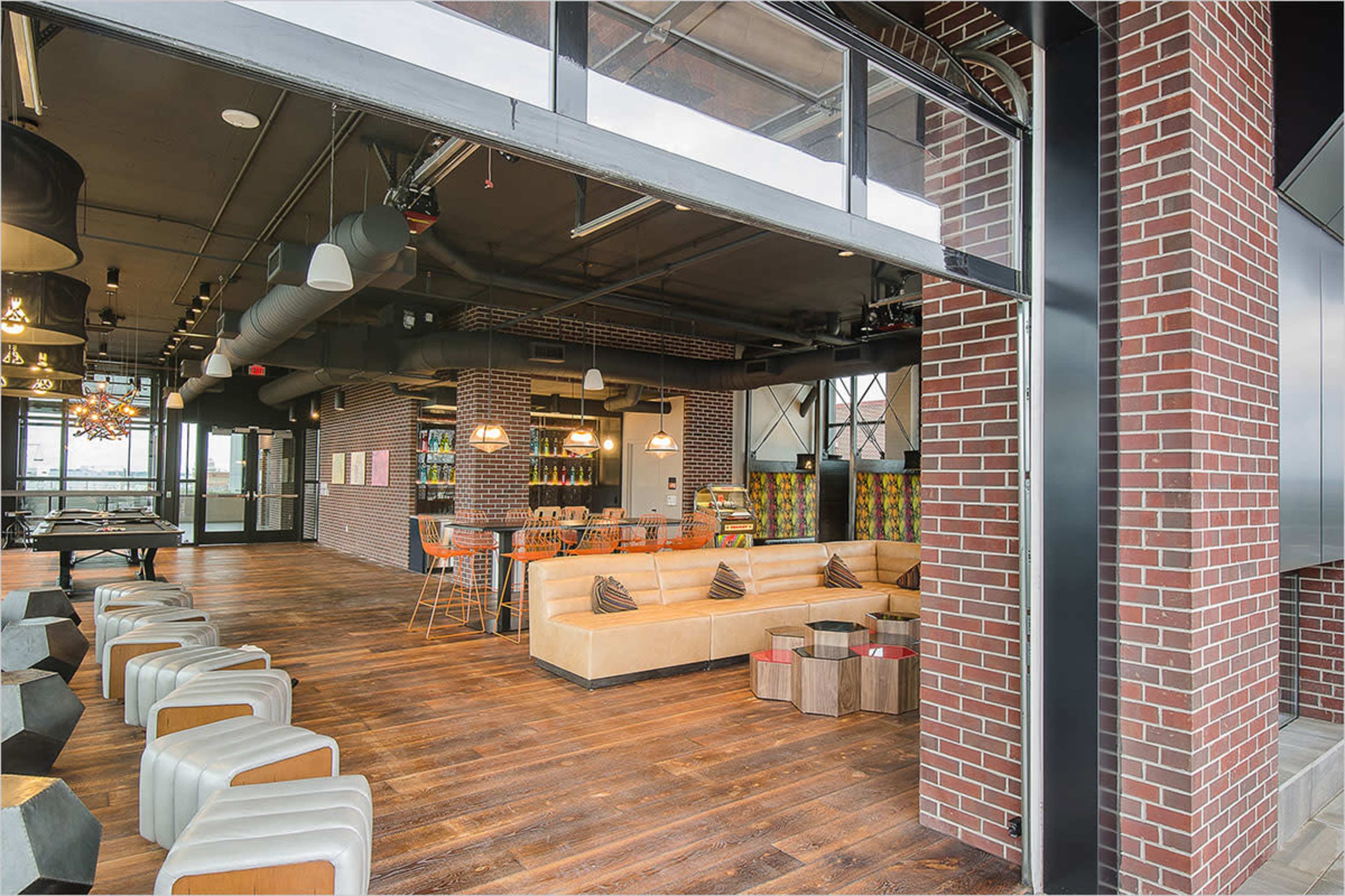 The image shows a modern interior space with a mix of seating areas, industrial-style decor, and a bar counter.