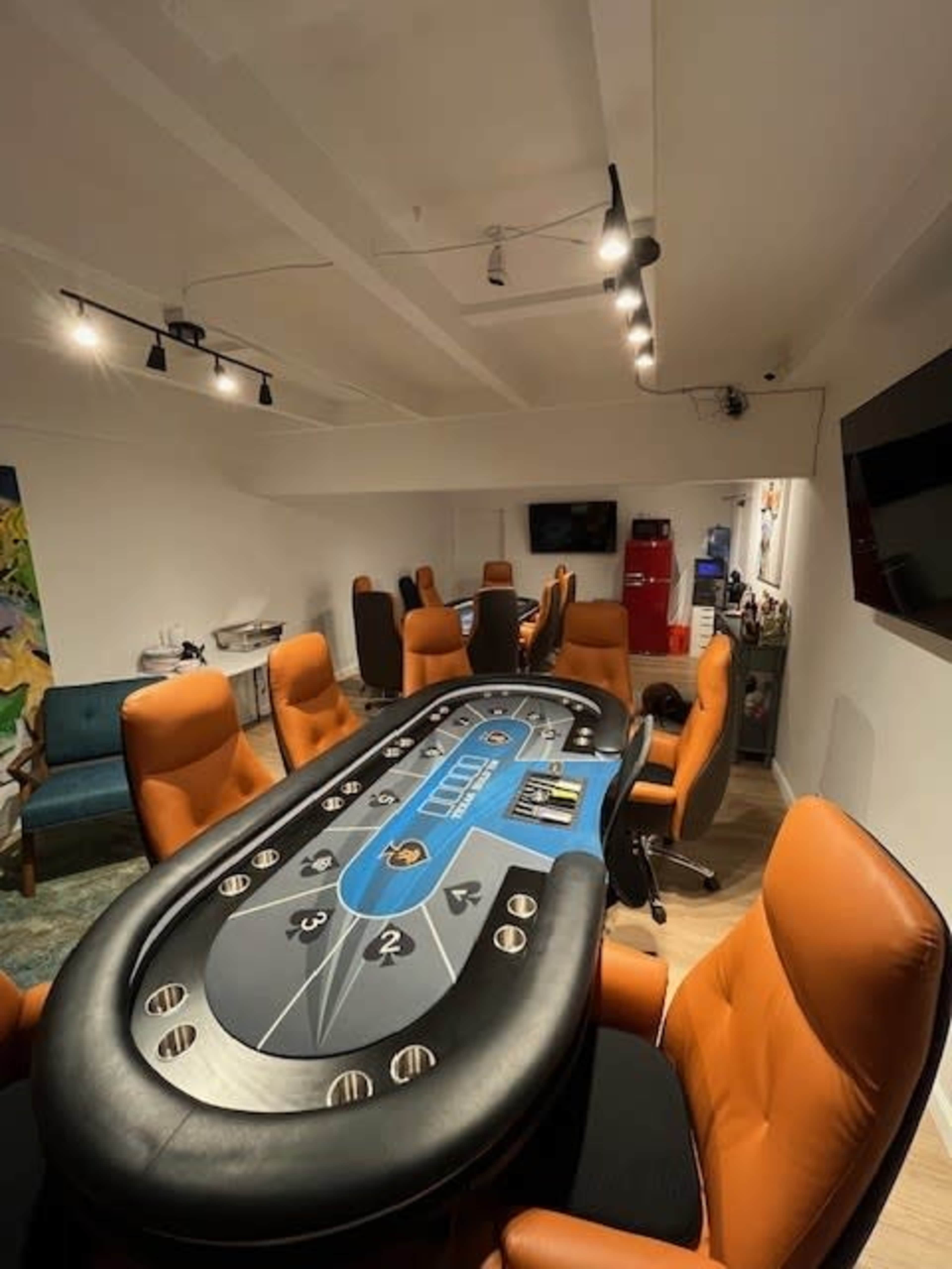 A poker table surrounded by several orange chairs in a well-lit room.