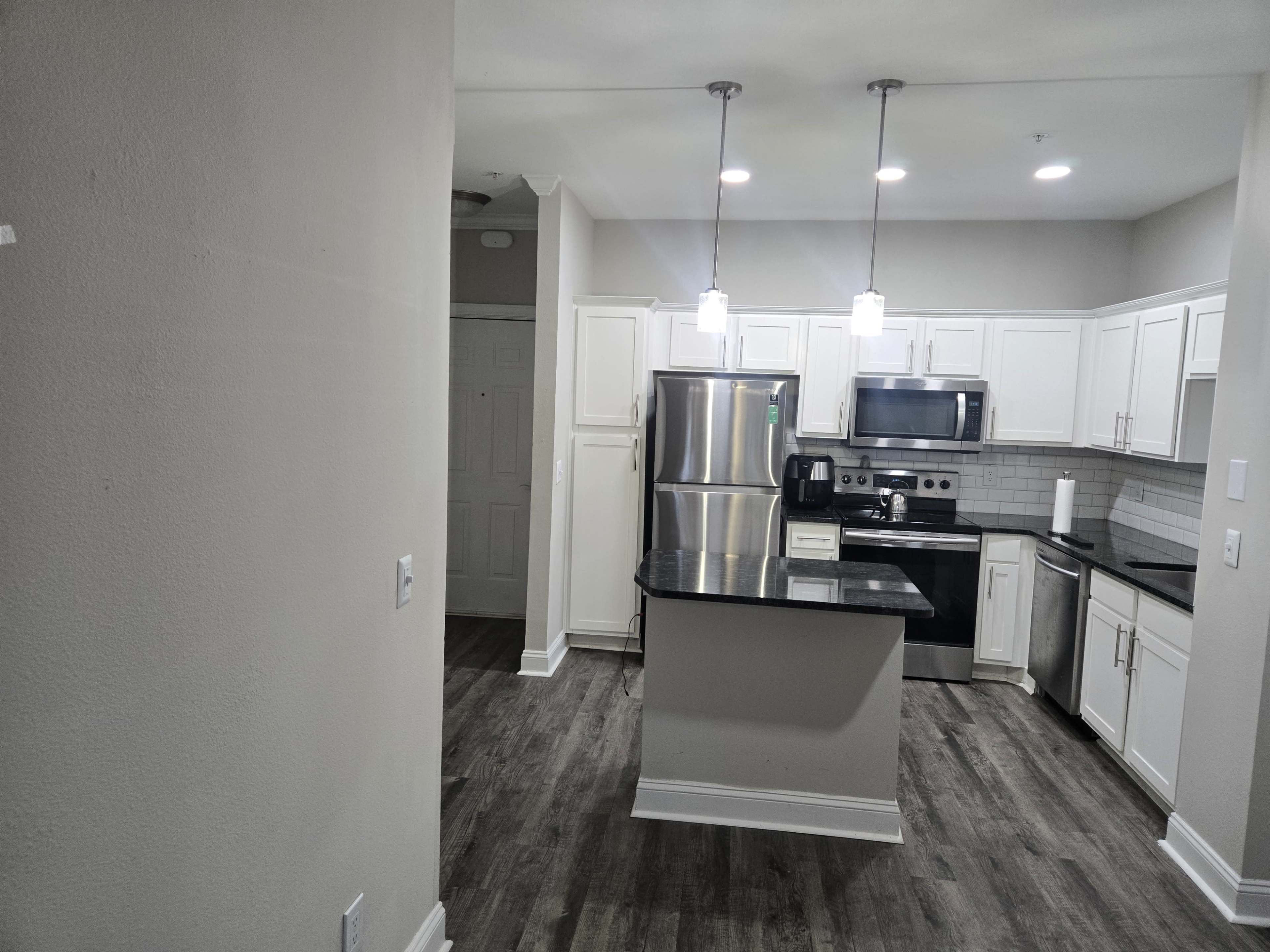 A modern kitchen features white cabinetry, stainless steel appliances, and a central island with pendant lighting.