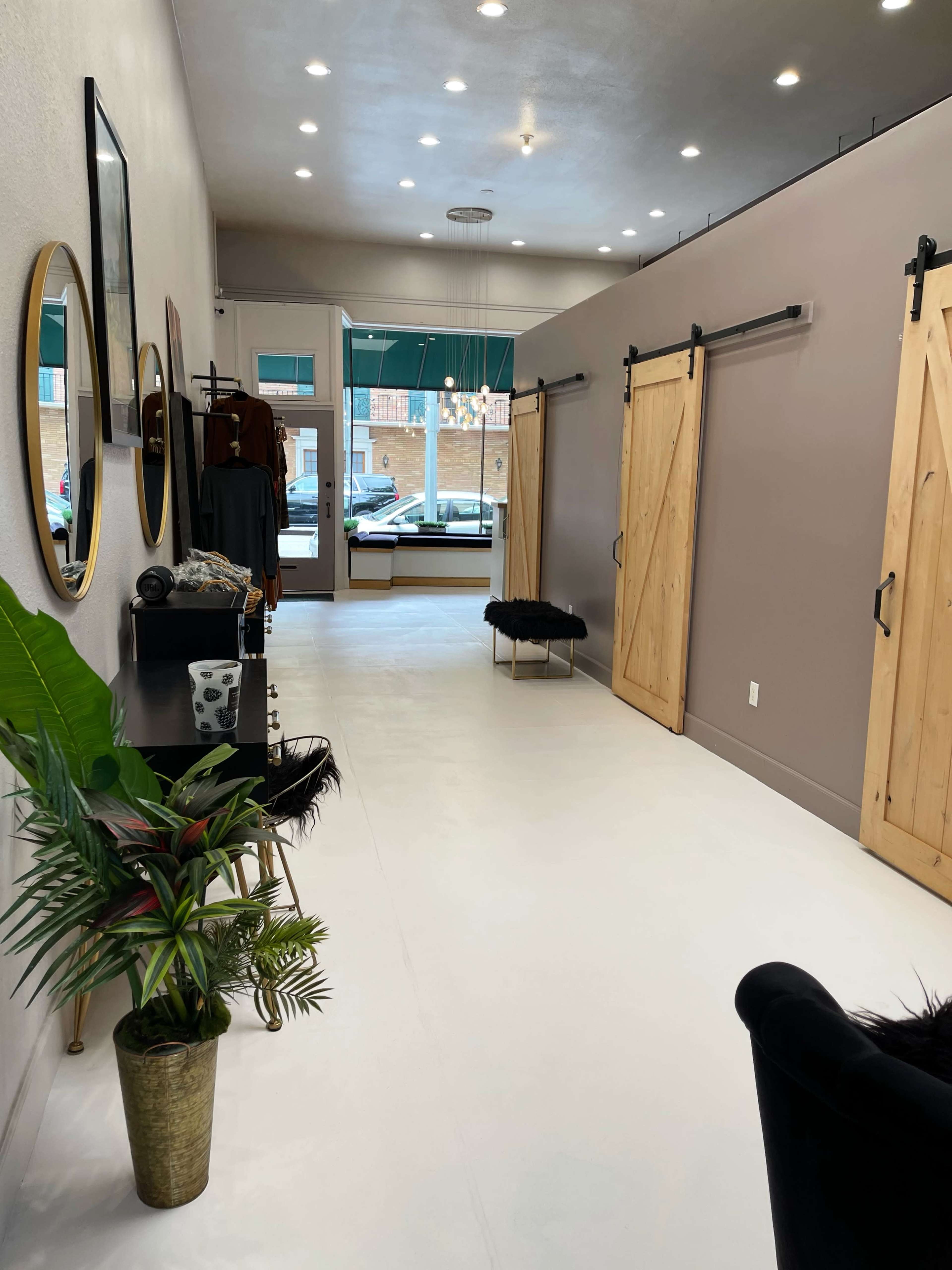 The image shows a narrow, well-lit hallway of a retail space with wooden sliding doors, a decorative plant in a pot, and minimalist furniture along the walls.