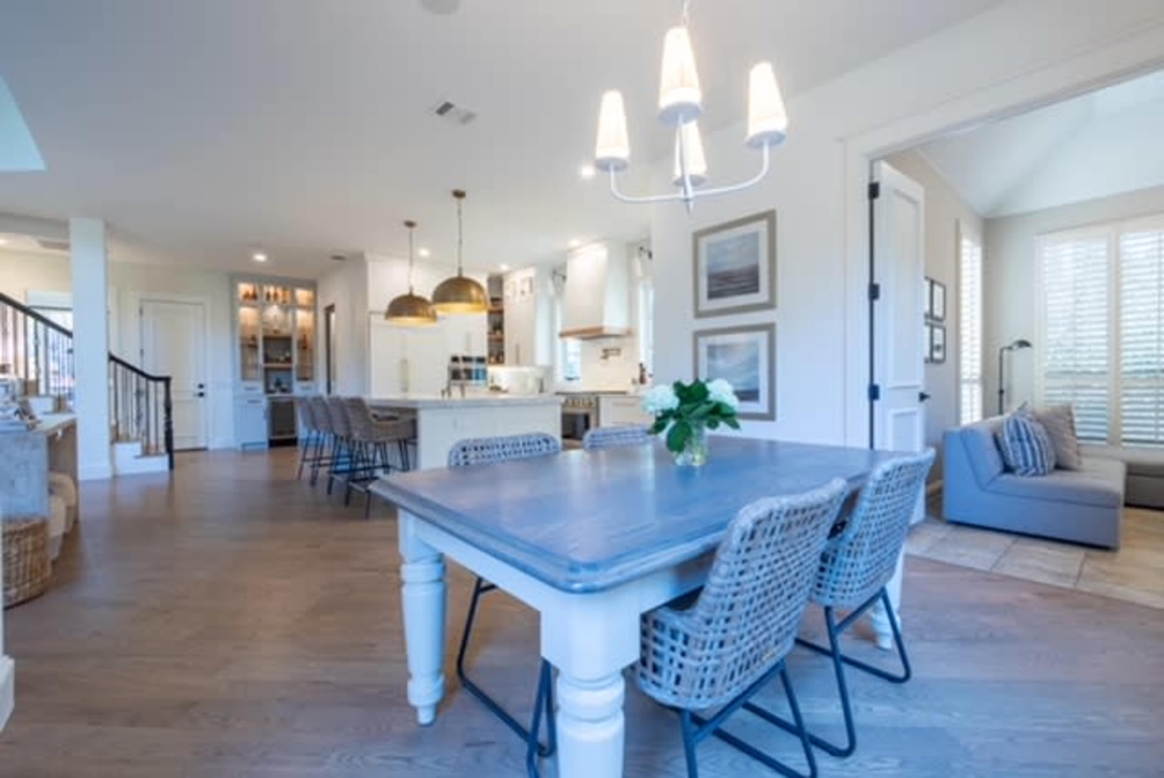 A well-lit dining area with a rustic table and woven chairs, opening to a modern kitchen and living space.