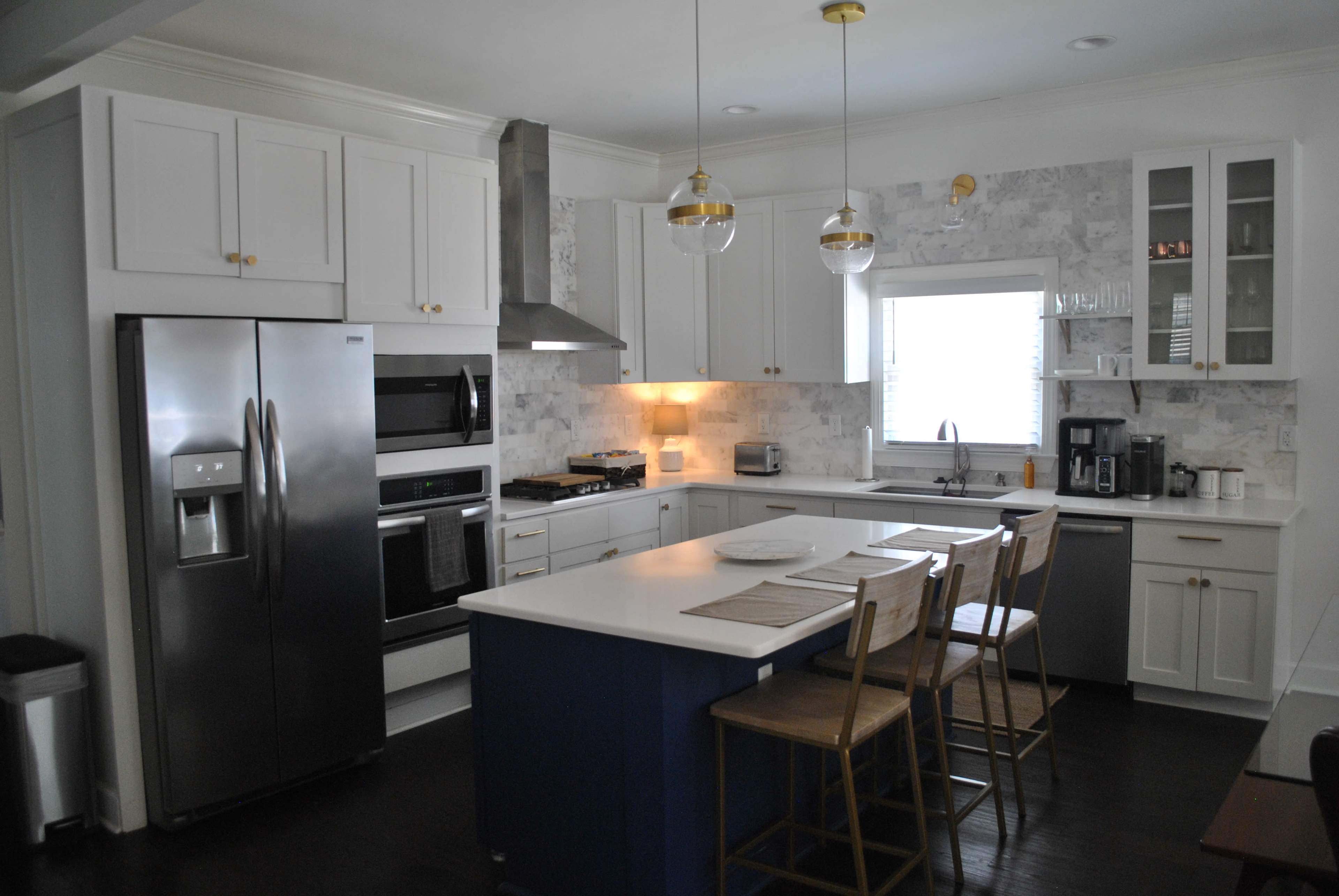 A modern kitchen featuring white cabinetry, a stainless steel refrigerator, and a central island with bar stools.